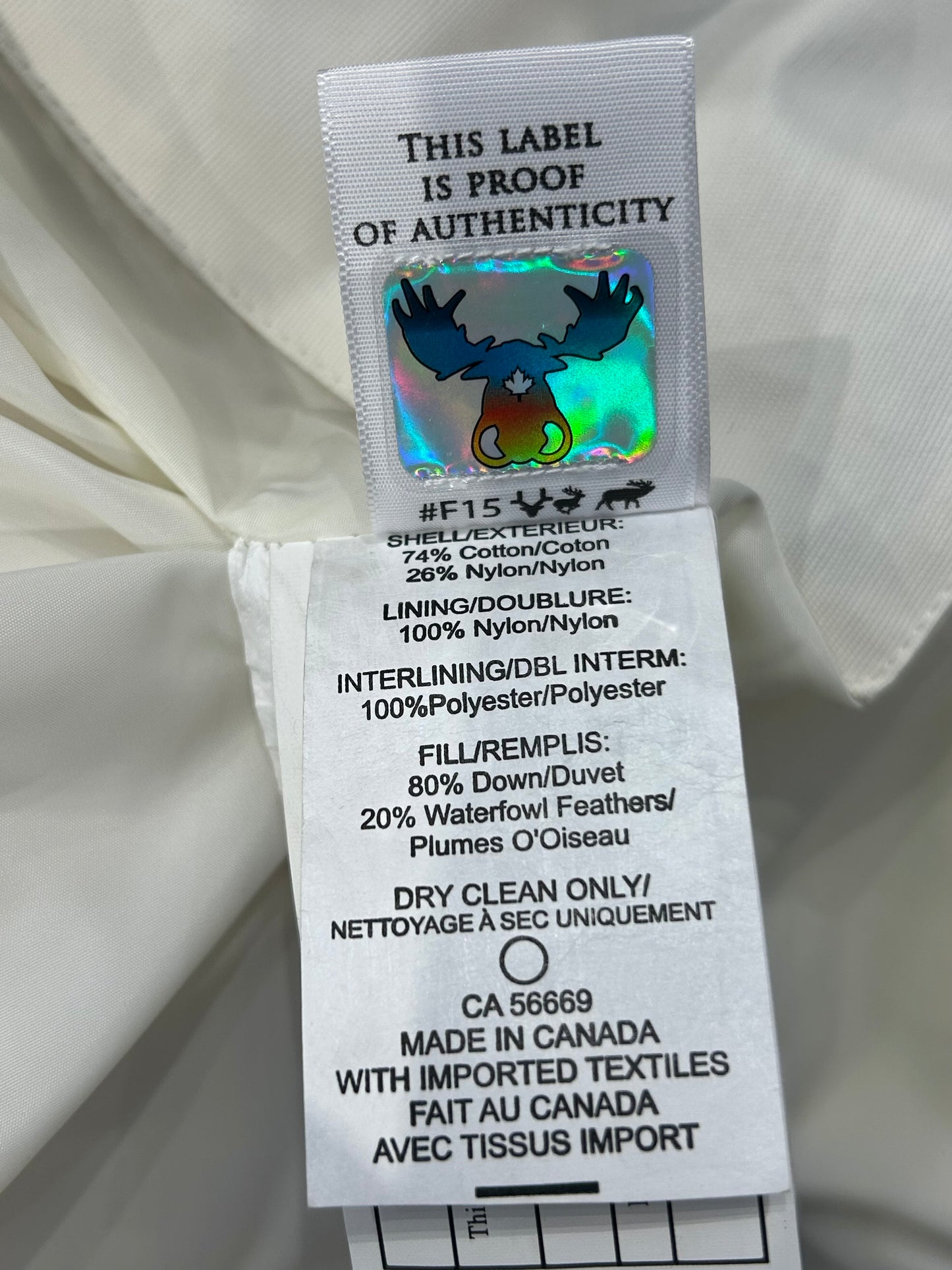 Moose Knuckle Women's White Down Puffer jacket authenticity label with holographic moose logo and material details.