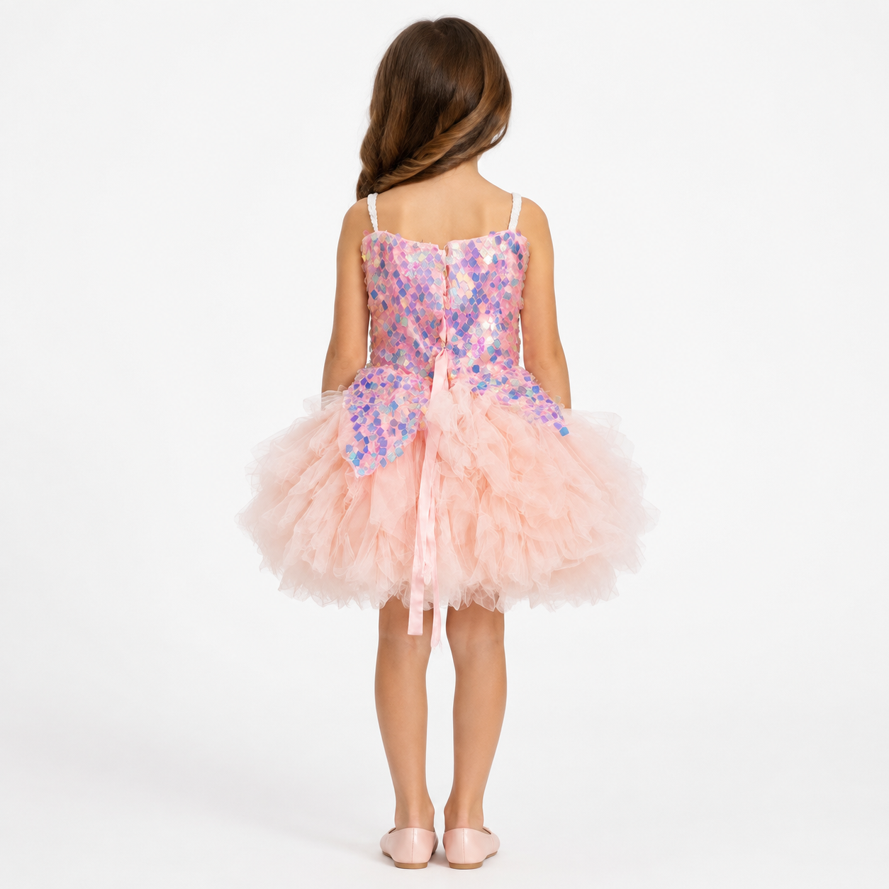 Girl wearing a blush-pink party dress with an iridescent sequin bodice, back bow, and voluminous layered tulle skirt.