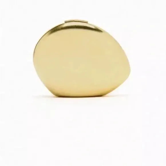 Minimalist gold metallic oblong clutch with a smooth, organic pebble-shaped design on a white background.