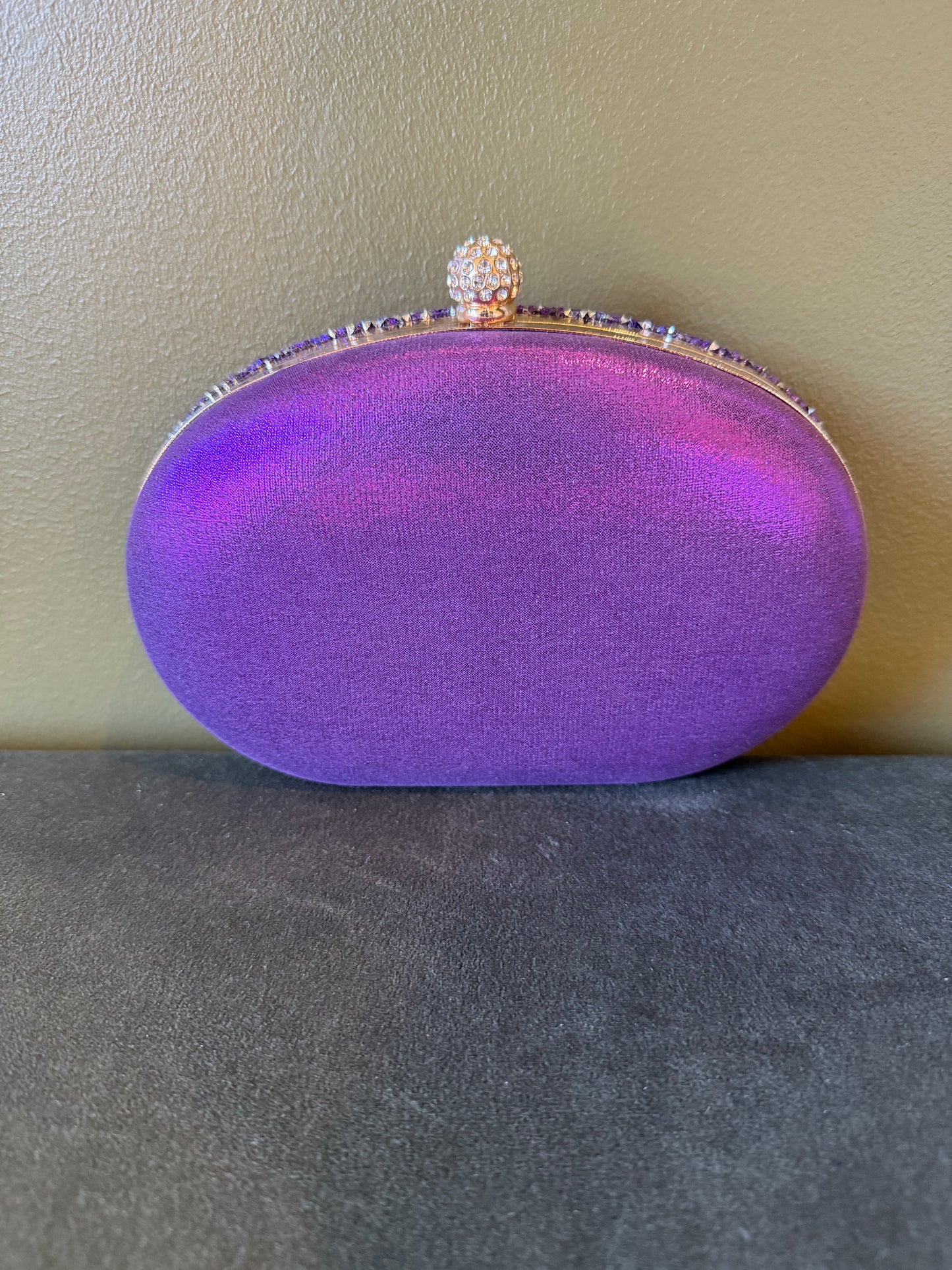 Oval purple satin clutch with a rhinestone-encrusted top clasp and decorative crystal trim.