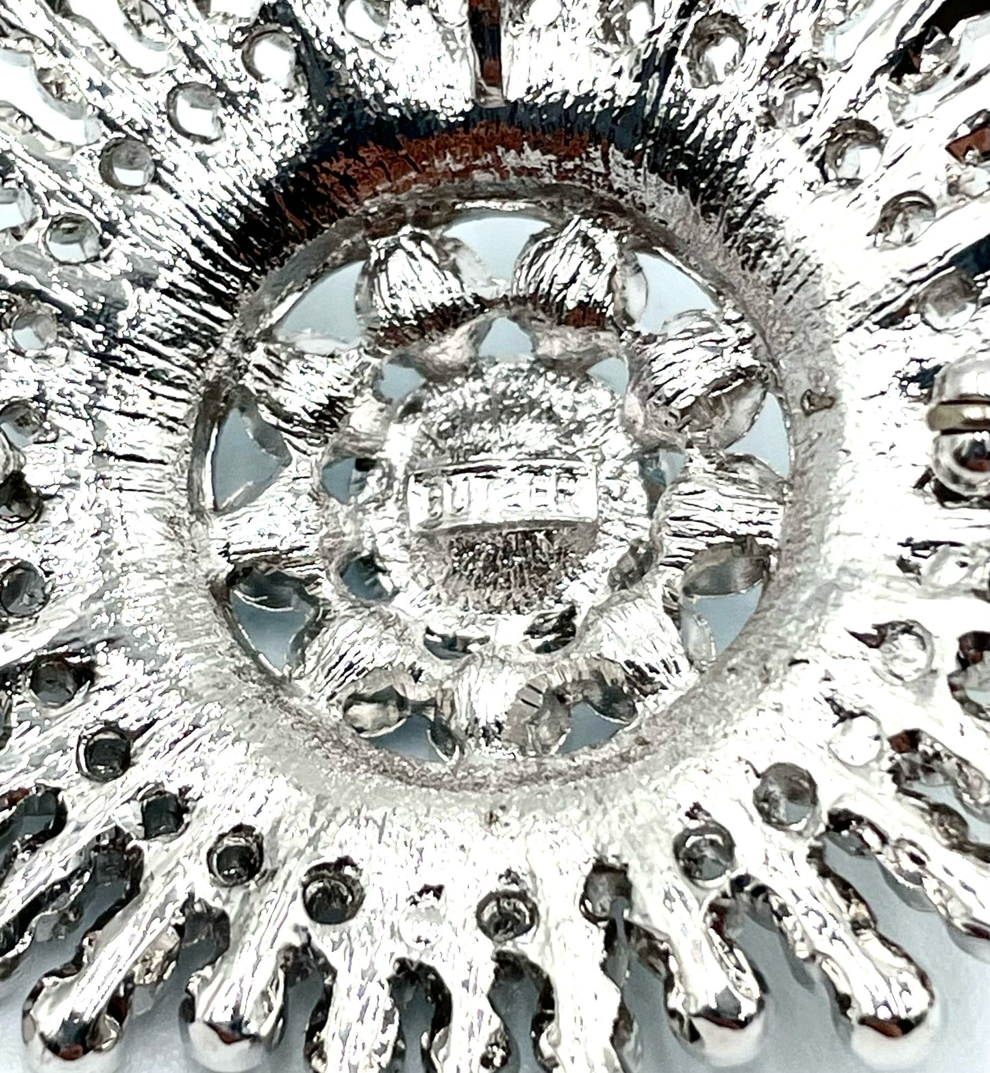 Back of a silver-toned Butler sunburst brooch with intricate metalwork and a pin clasp.