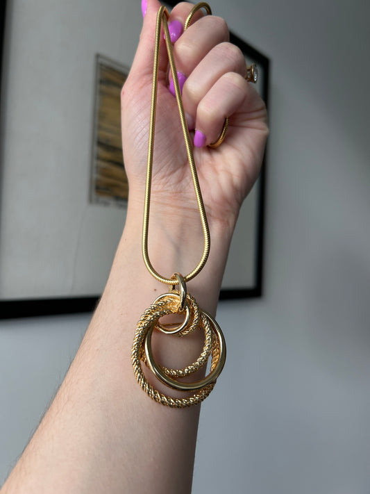 Hand holding a 1970s gold-toned knot pendant necklace on a snake chain.