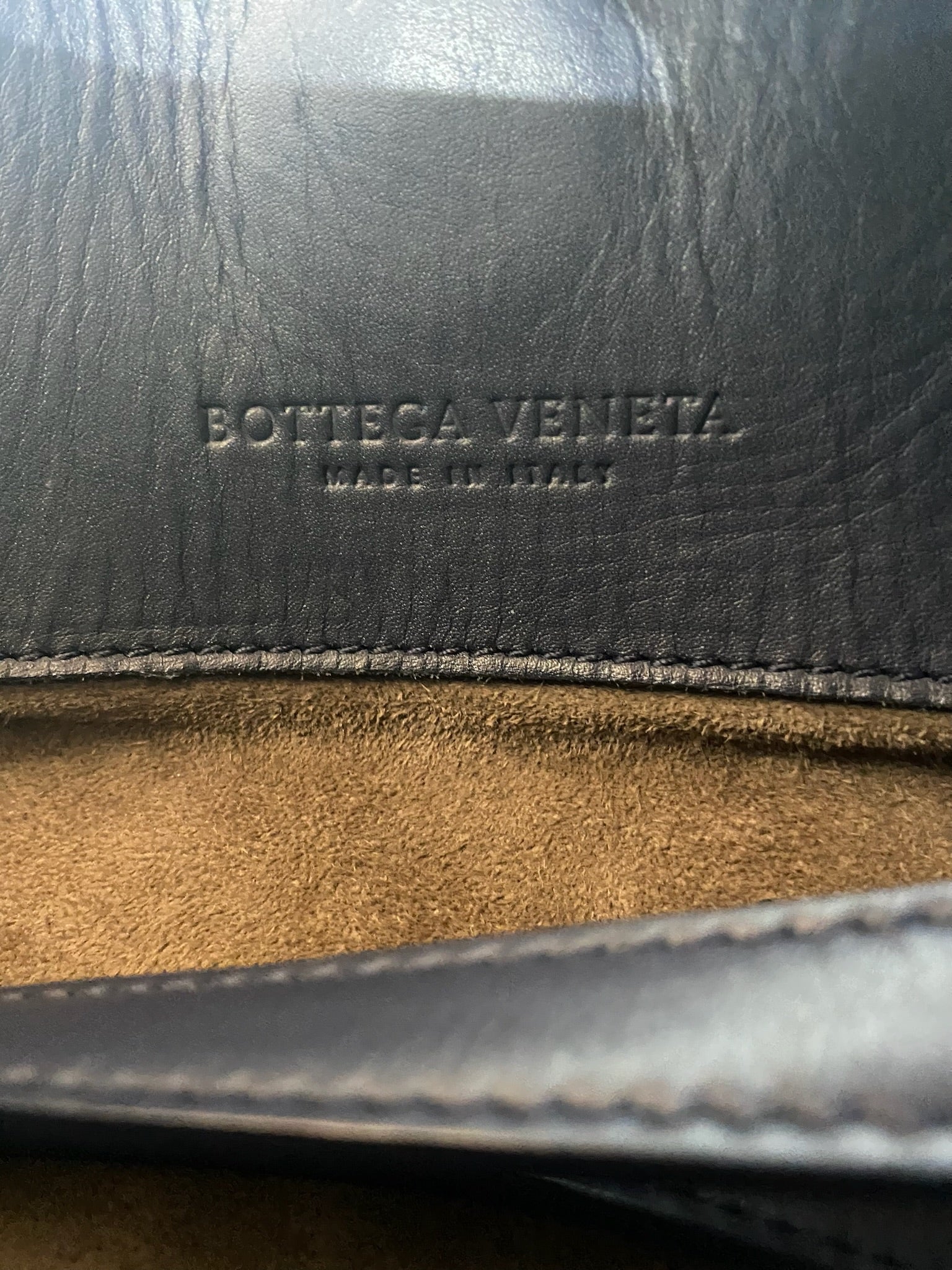 Bottega Veneta "Made in Italy" embossed on dark leather, with a brown suede interior.