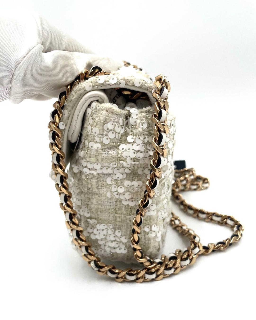 Karl Lagerfeld cream sequin crossbody bag with gold chain strap and textured fabric finish held by a gloved hand.