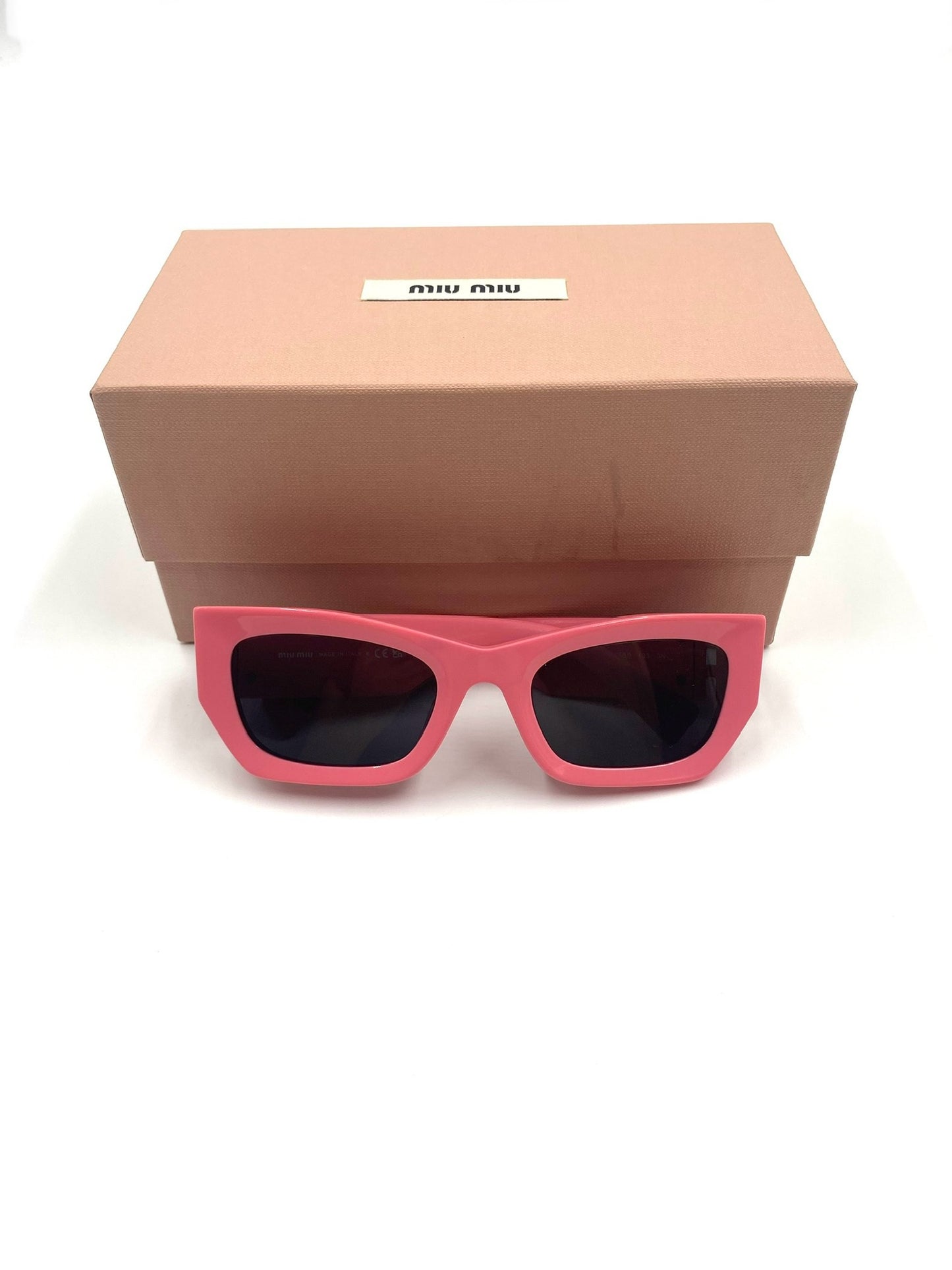 Miu Miu pink rectangular acetate sunglasses with grey tinted lenses, in front of a matching pink box.