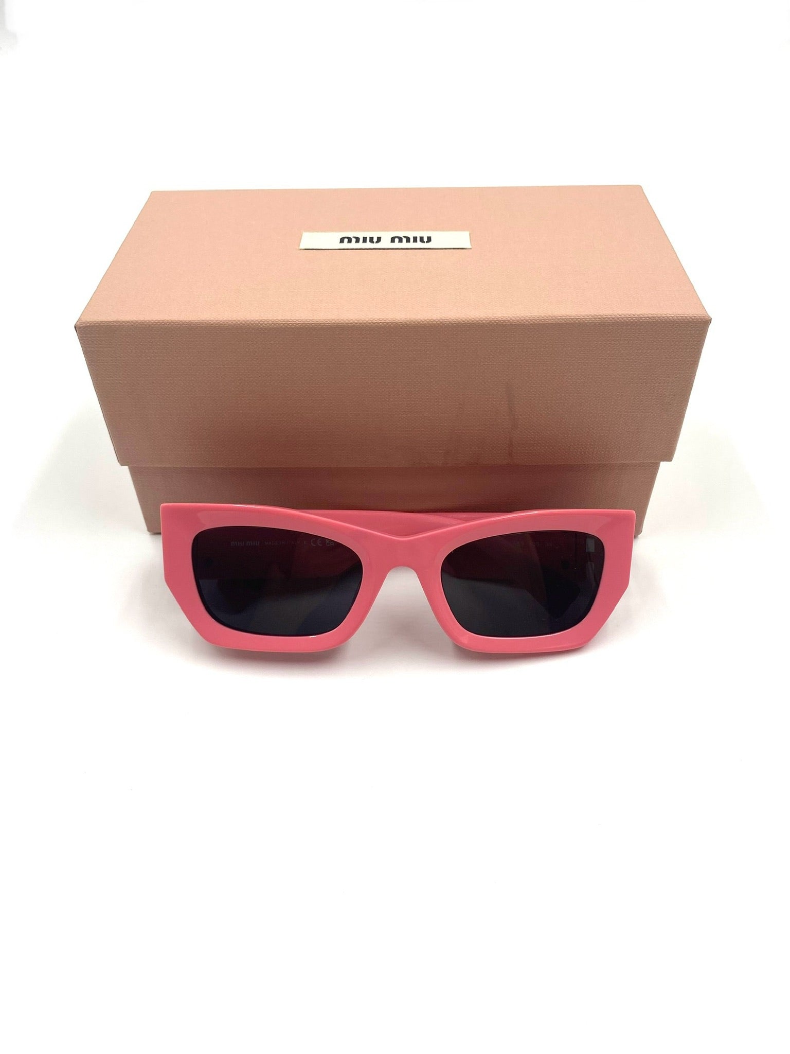 Miu Miu pink rectangular acetate sunglasses with grey tinted lenses, in front of a matching pink box.