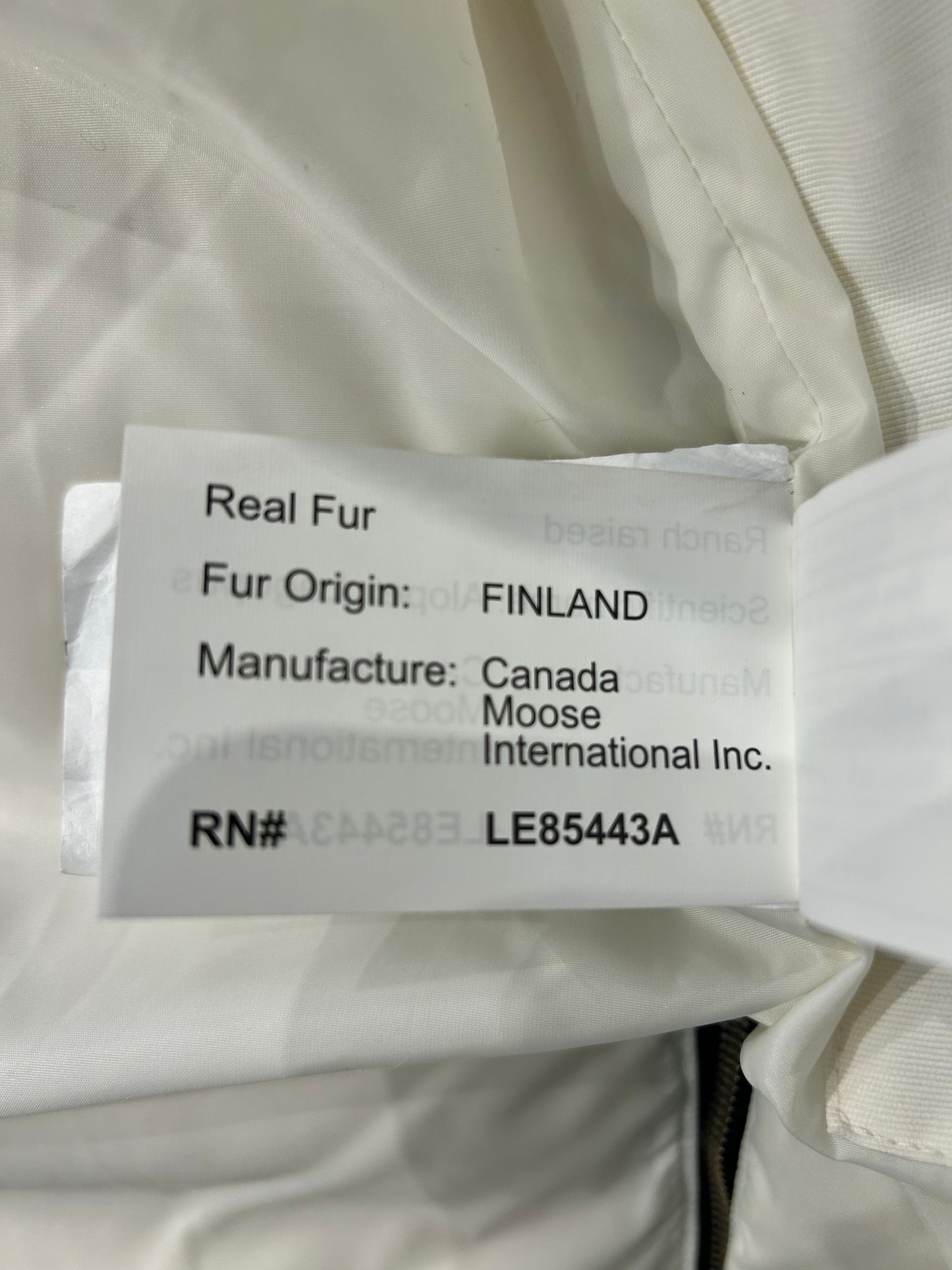 Close-up of a white Moose Knuckle down puffer jacket's tag, showing "Real Fur" and "Fur Origin: FINLAND.