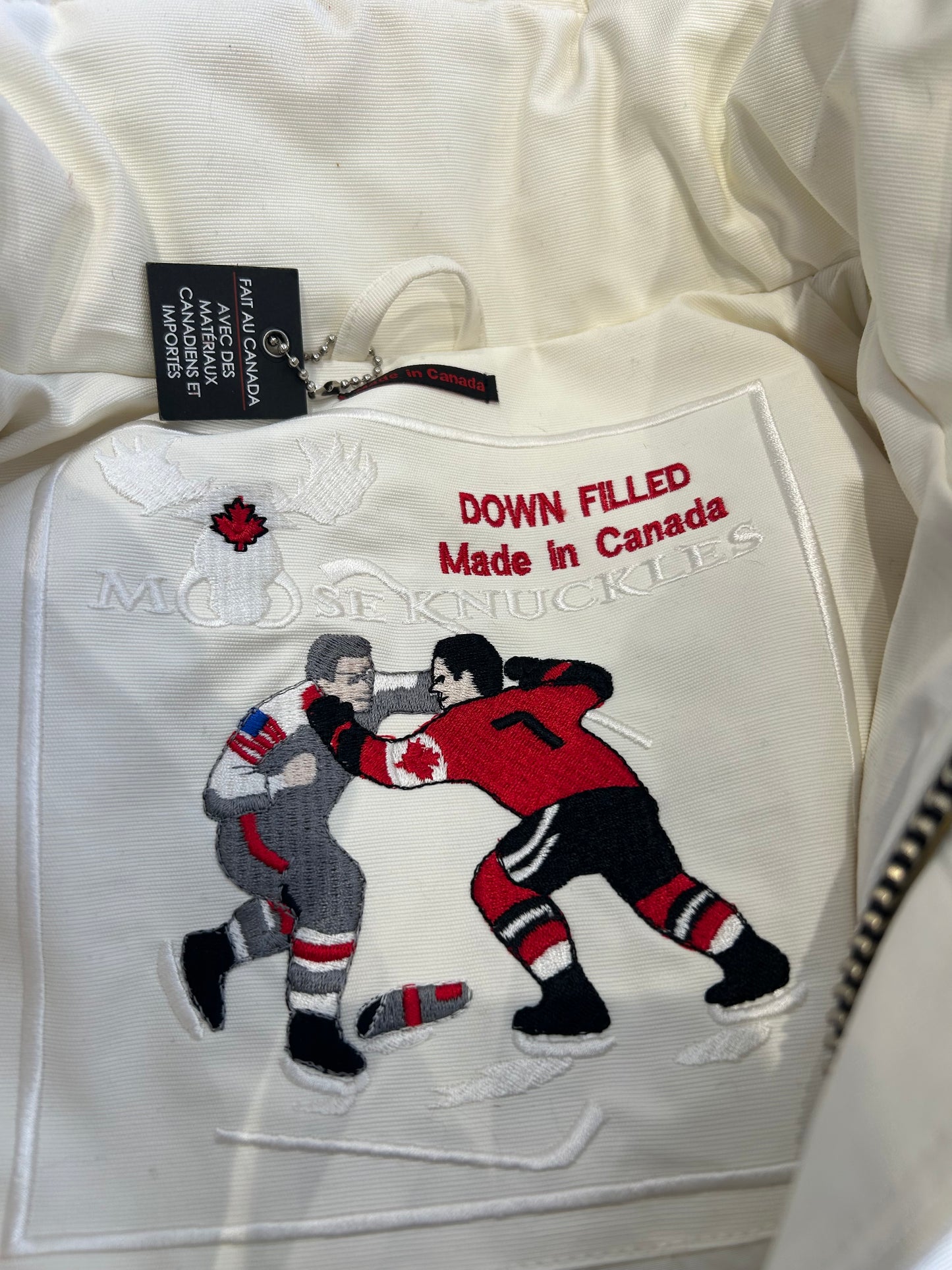 Moose Knuckle Women's White Down Puffer, XS, with "Down Filled Made in Canada" embroidery and hockey players.