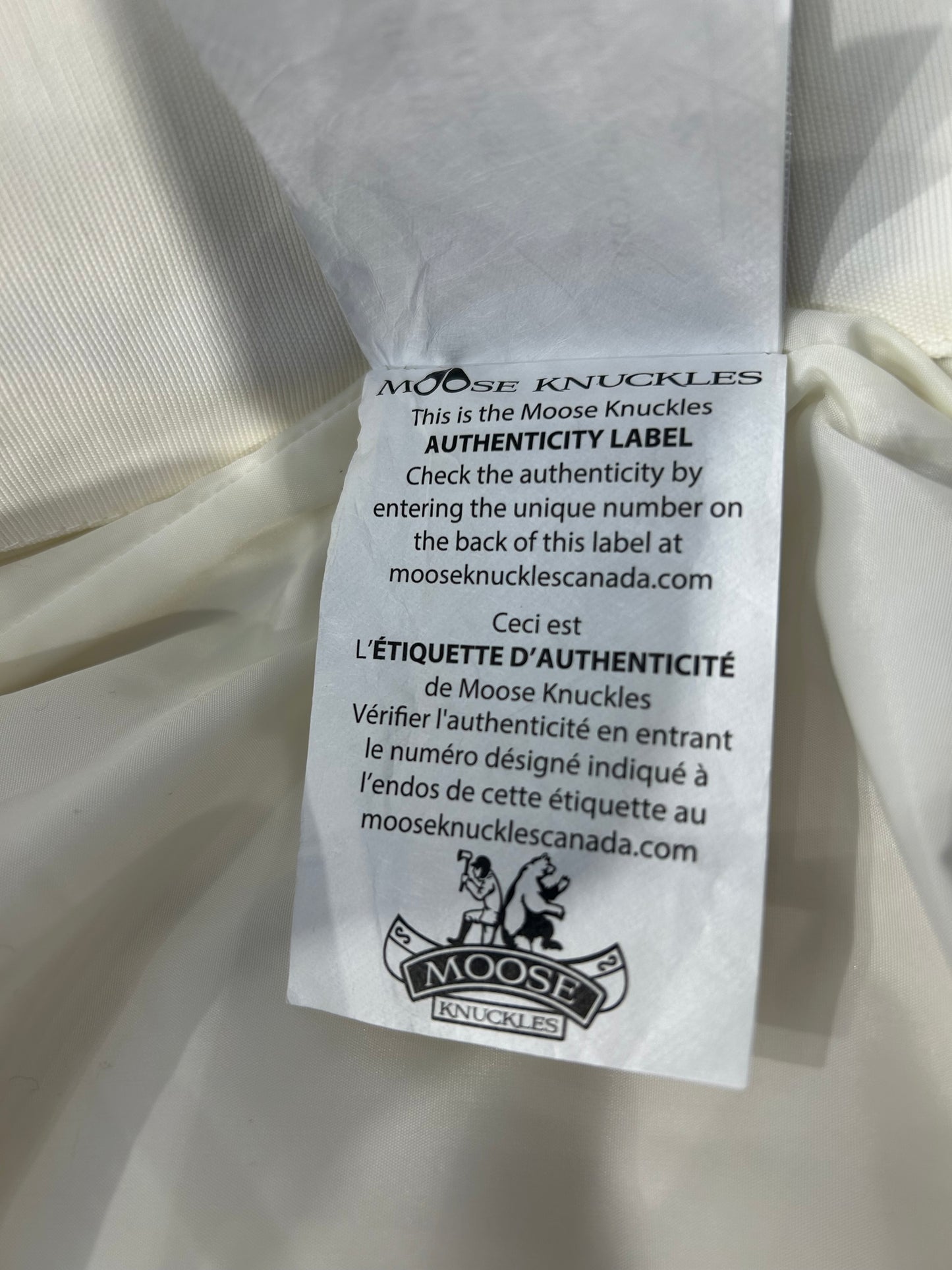 Moose Knuckles authenticity label on a white down puffer jacket.