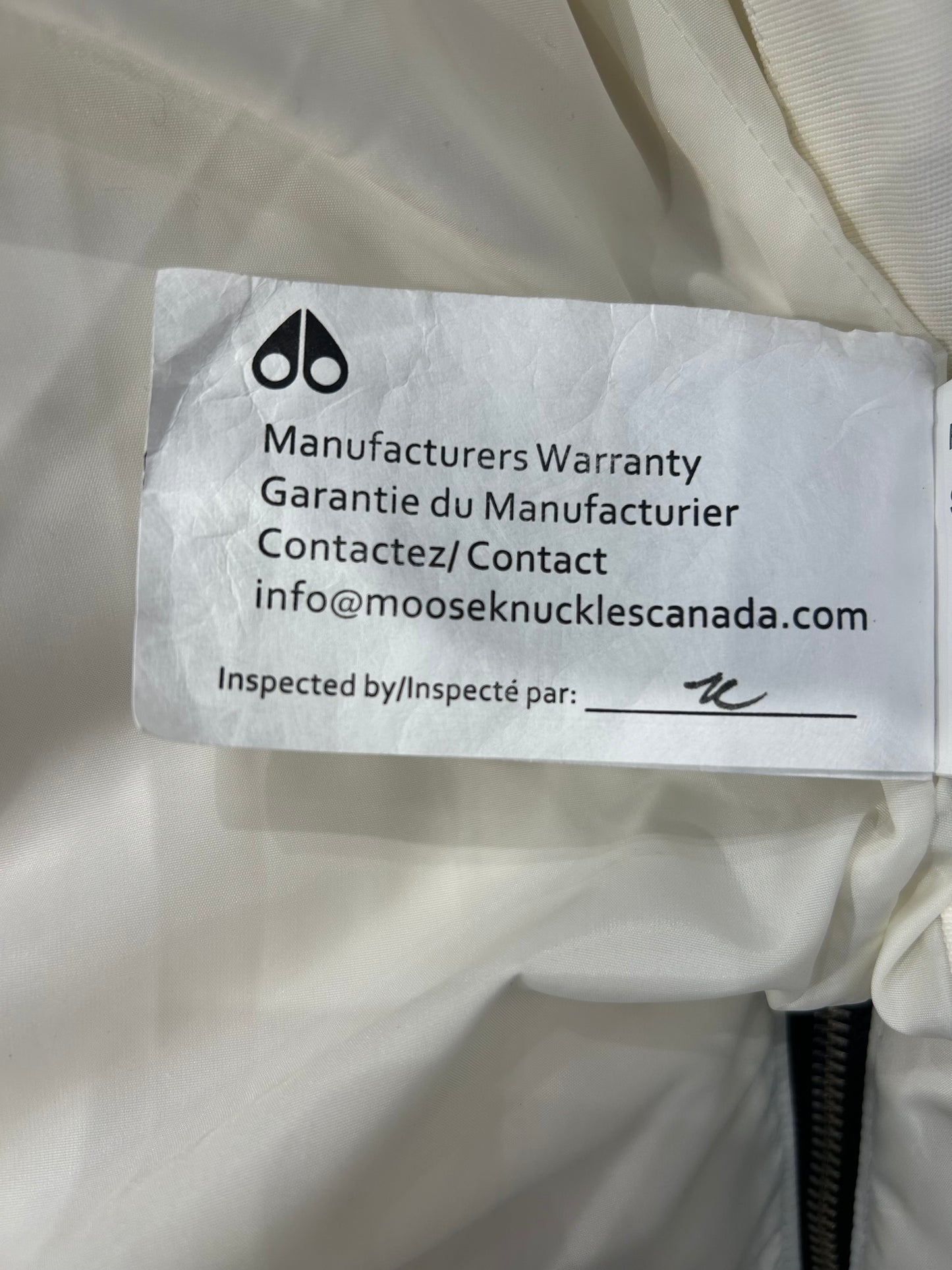 Moose Knuckle white down puffer jacket tag with warranty info and brand logo.