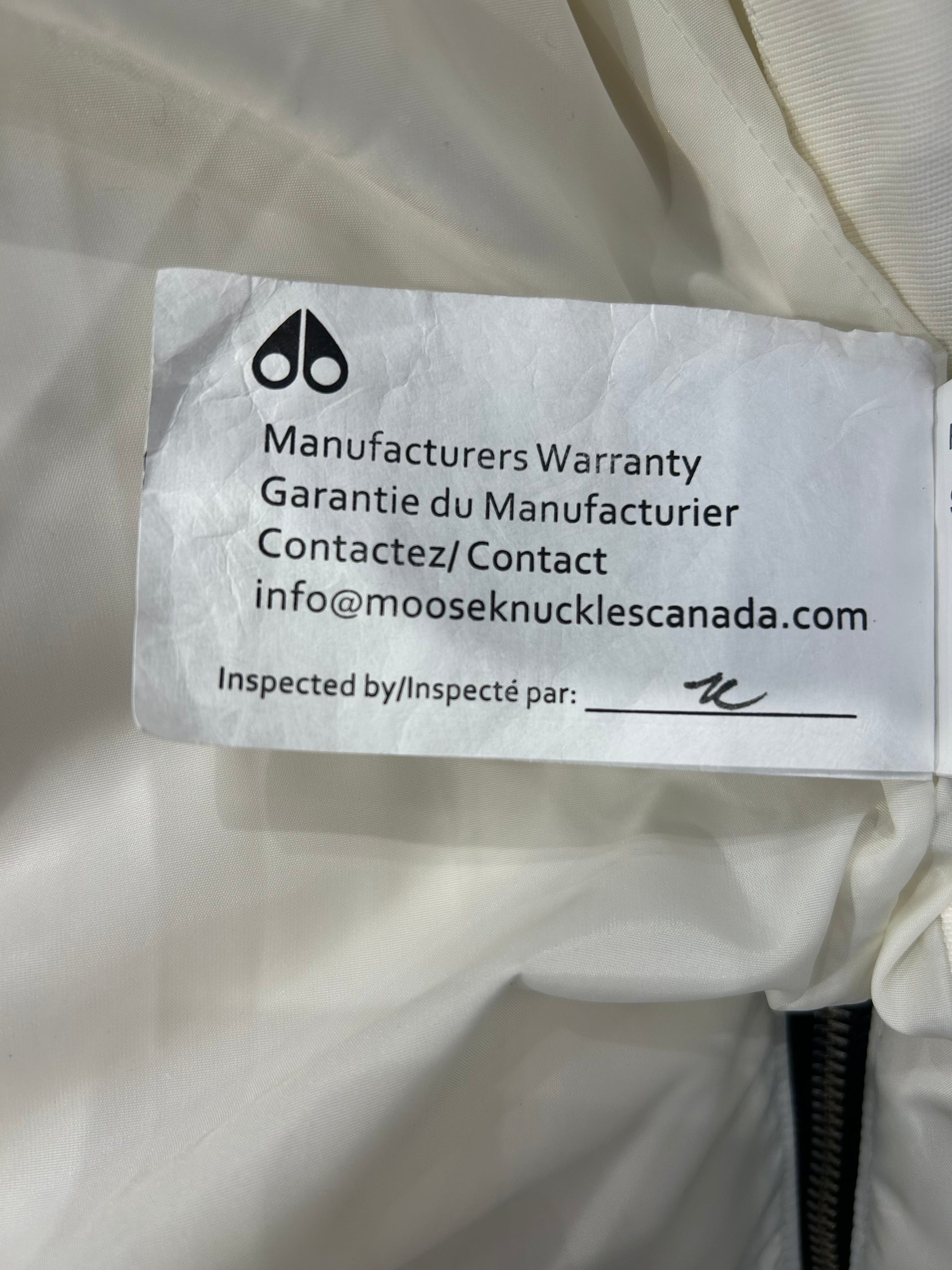 Moose Knuckle white down puffer jacket tag with warranty info and brand logo.