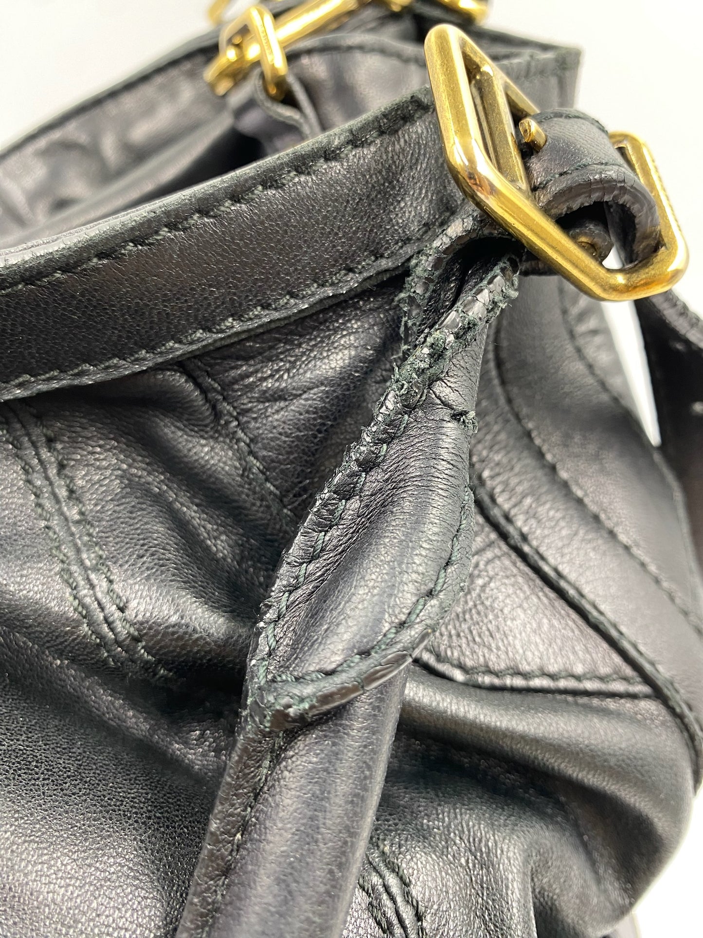 Close-up of a black leather Burberry handbag handle with visible wear and gold hardware.