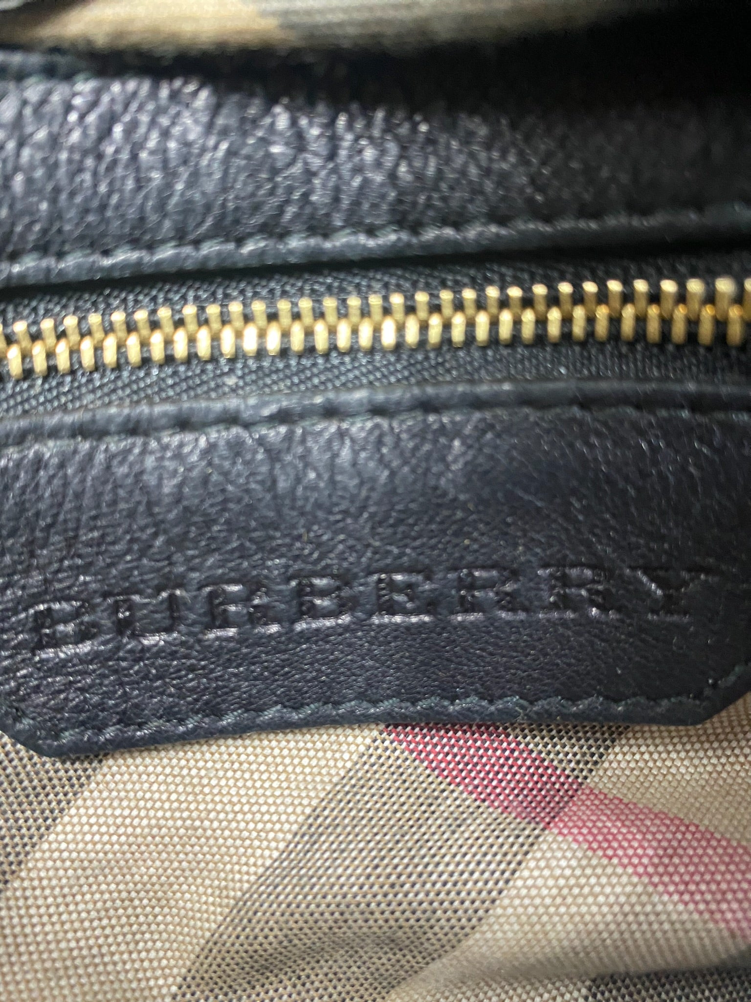 Close-up of Burberry black leather handbag with gold zipper and classic checked lining.