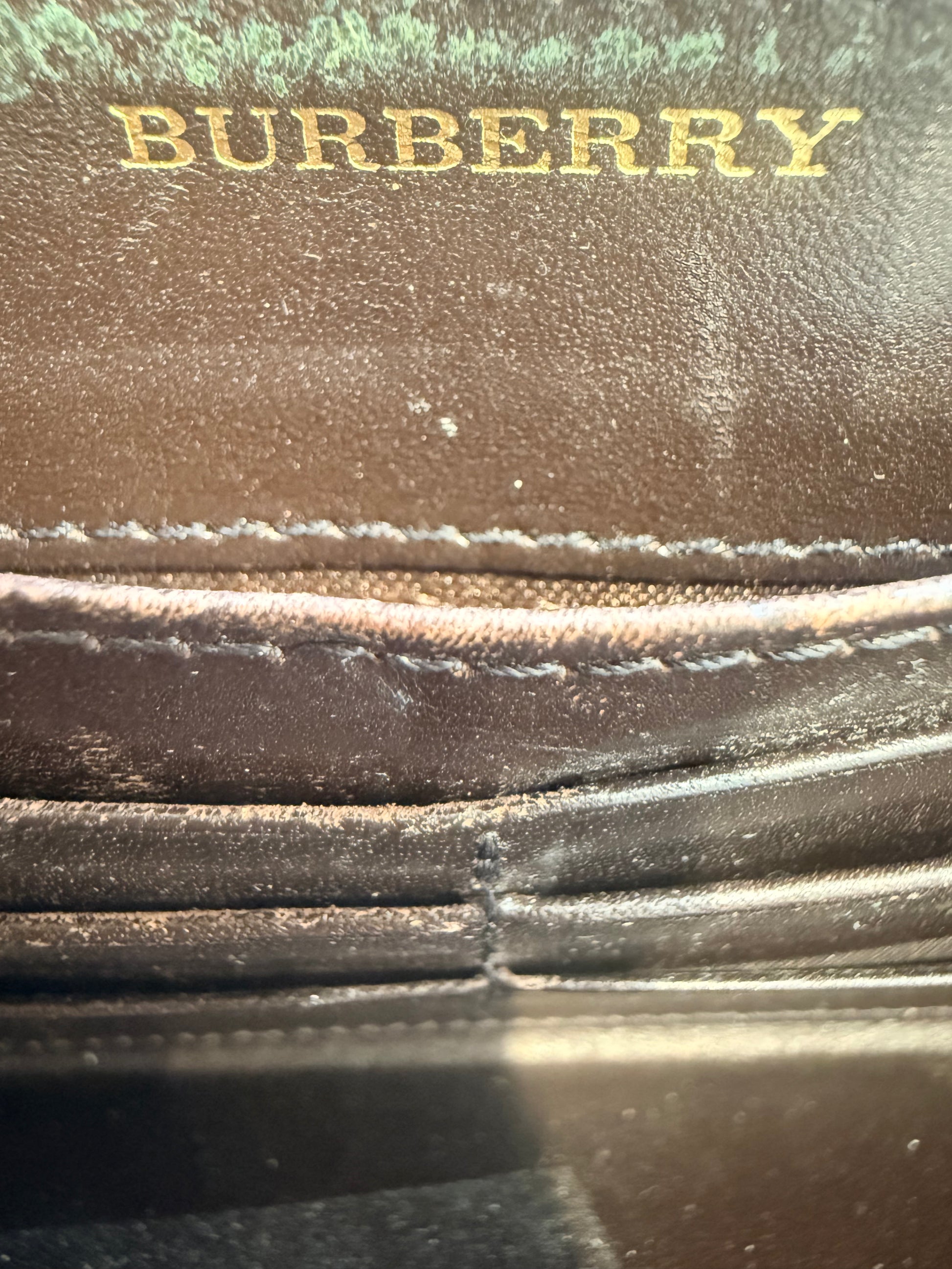Interior of a black leather Burberry continental wallet featuring gold embossed branding and card slot compartments.