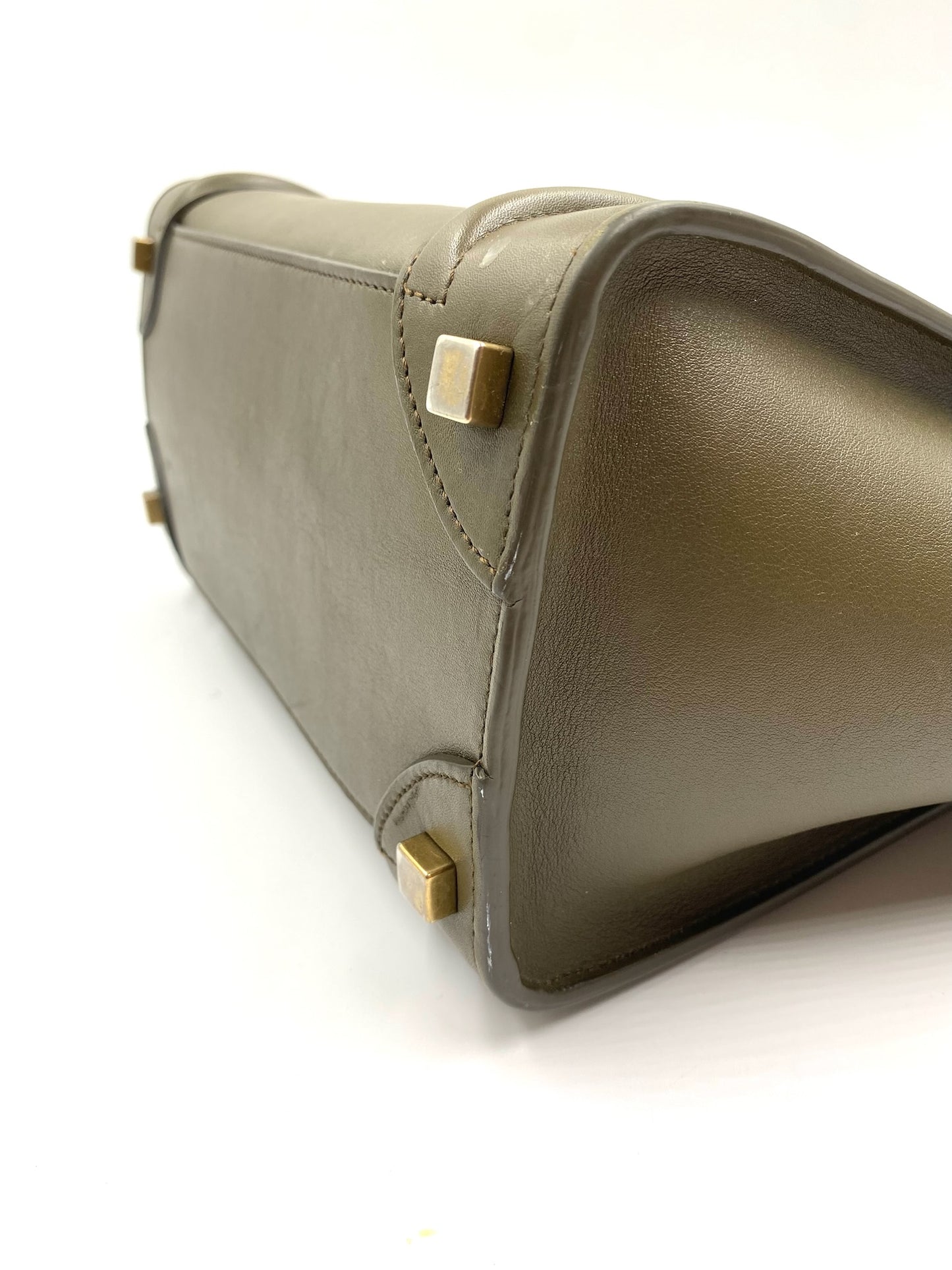 Celine Olive Calfskin Micro Luggage Tote bottom with gold-tone hardware feet on a white surface.