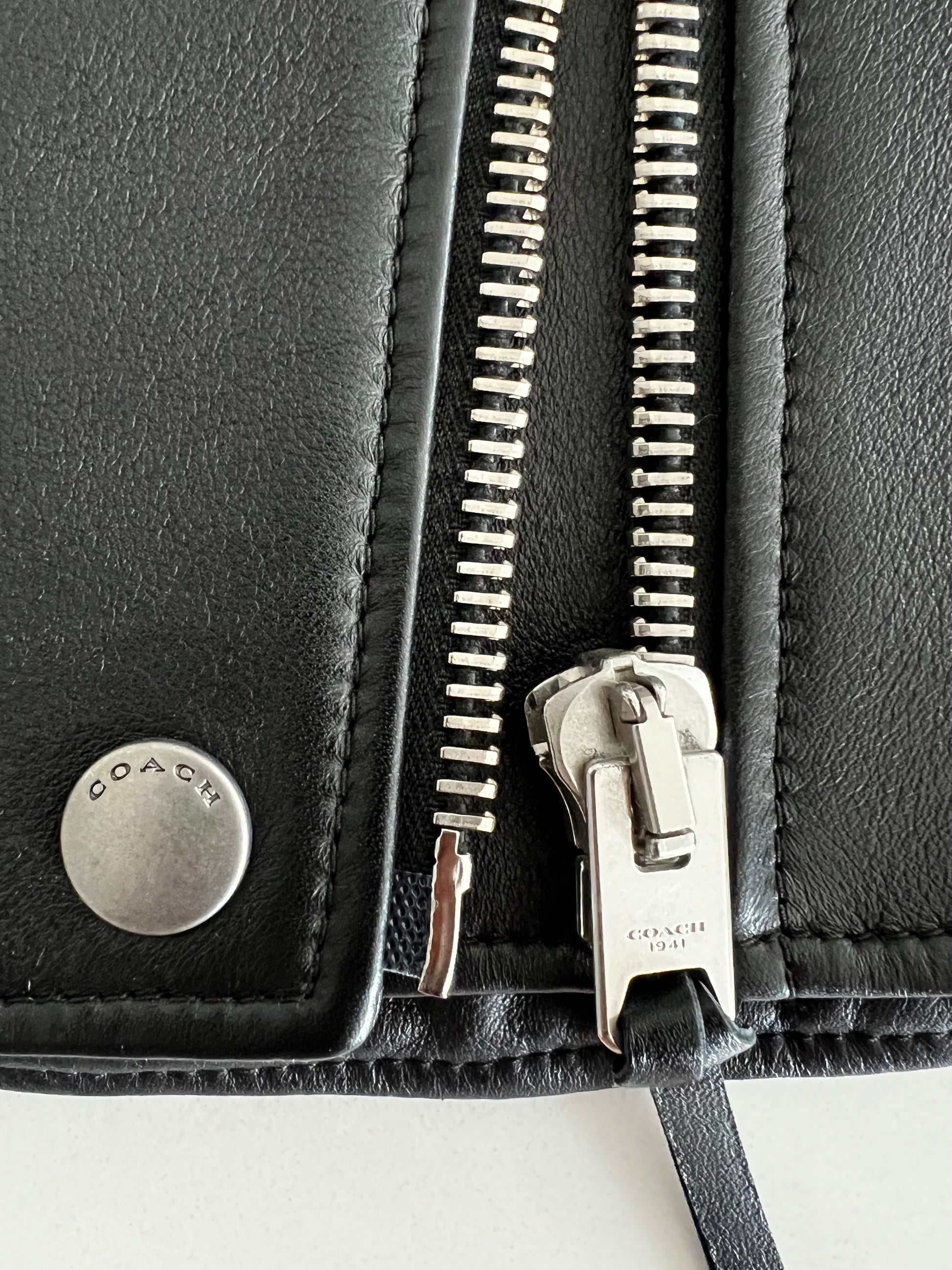 Coach 1941 black leather biker vest, close-up of silver zipper and snap with "COACH" logo.
