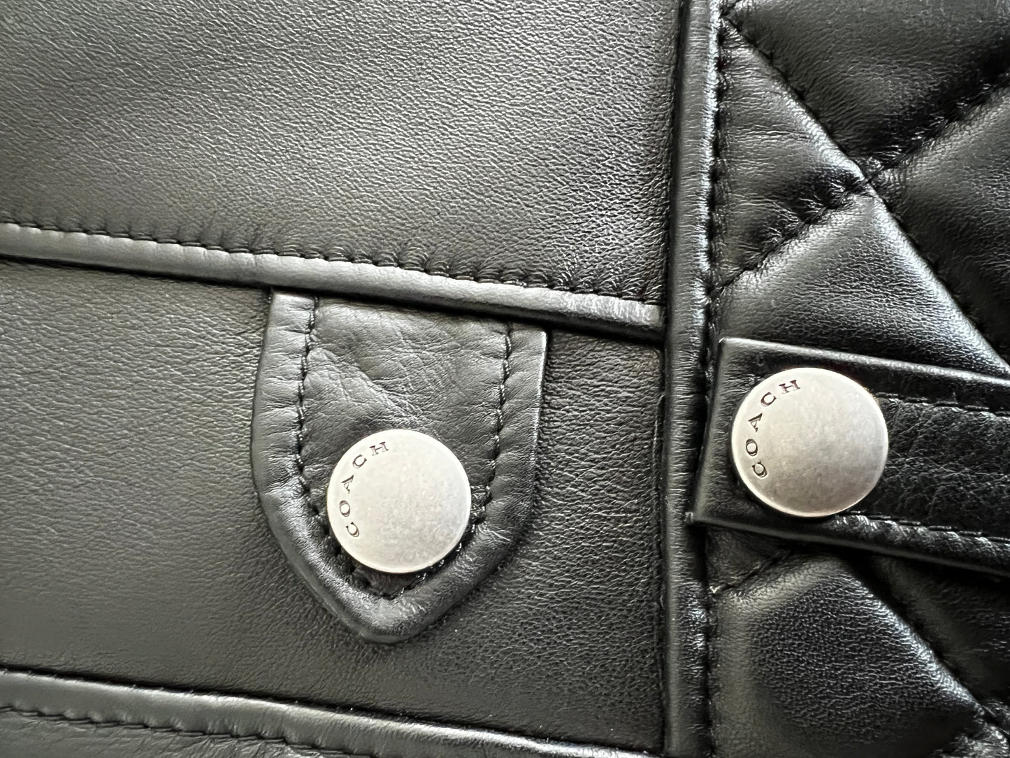 Close-up of a black leather Coach 1941 biker vest with quilted details and silver "COACH" buttons.