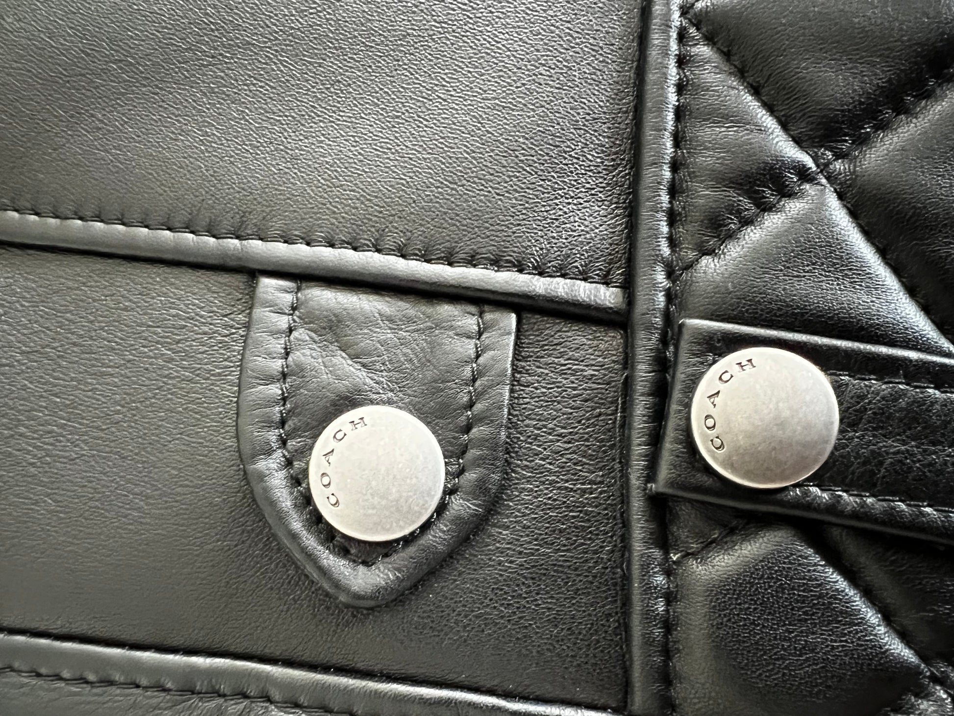 Close-up of a black leather Coach 1941 biker vest with quilted details and silver "COACH" buttons.