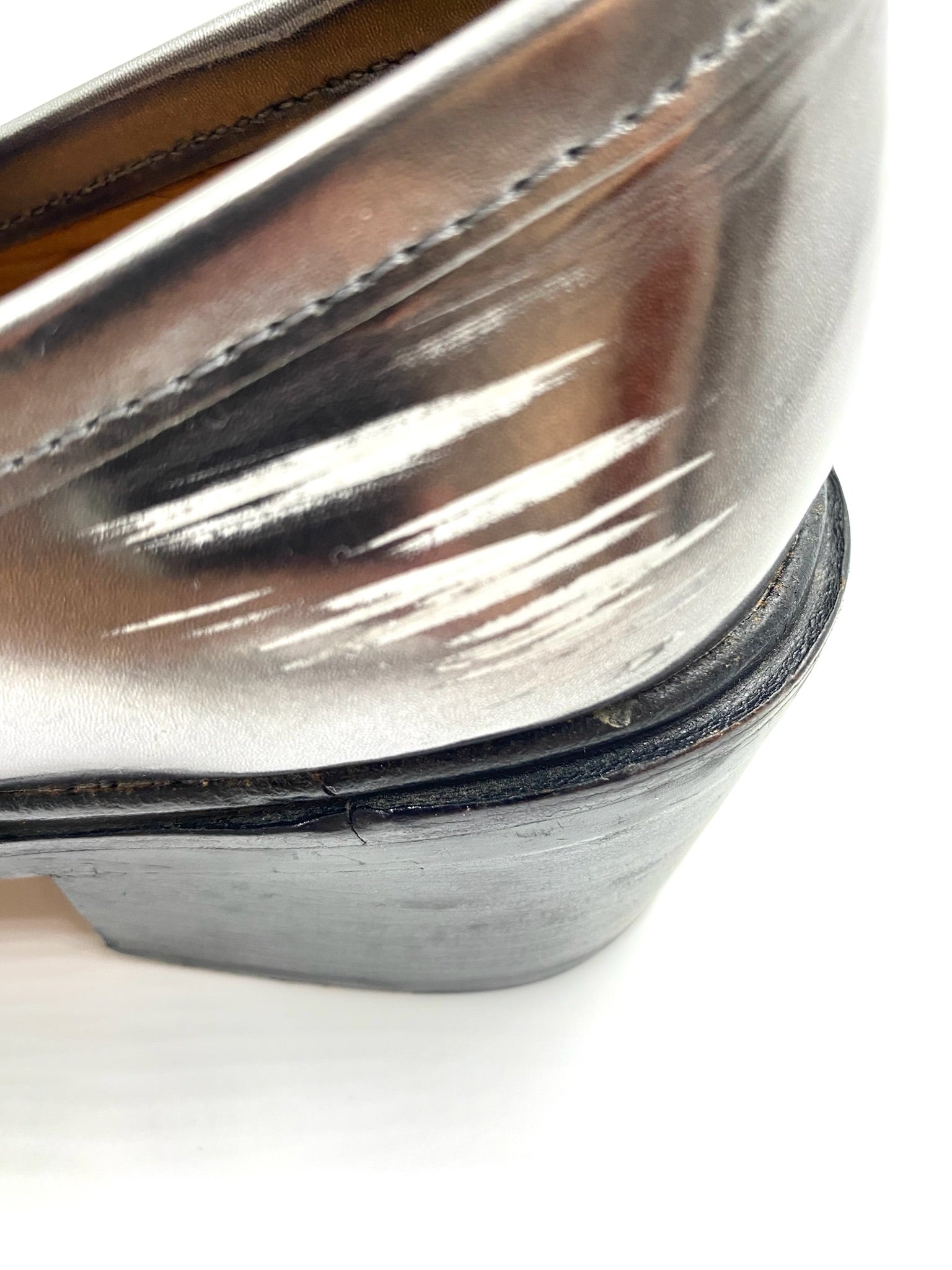 Close-up of a Coach Grey Metallic Loafer, size 8, showing scratches and wear on the metallic leather heel.