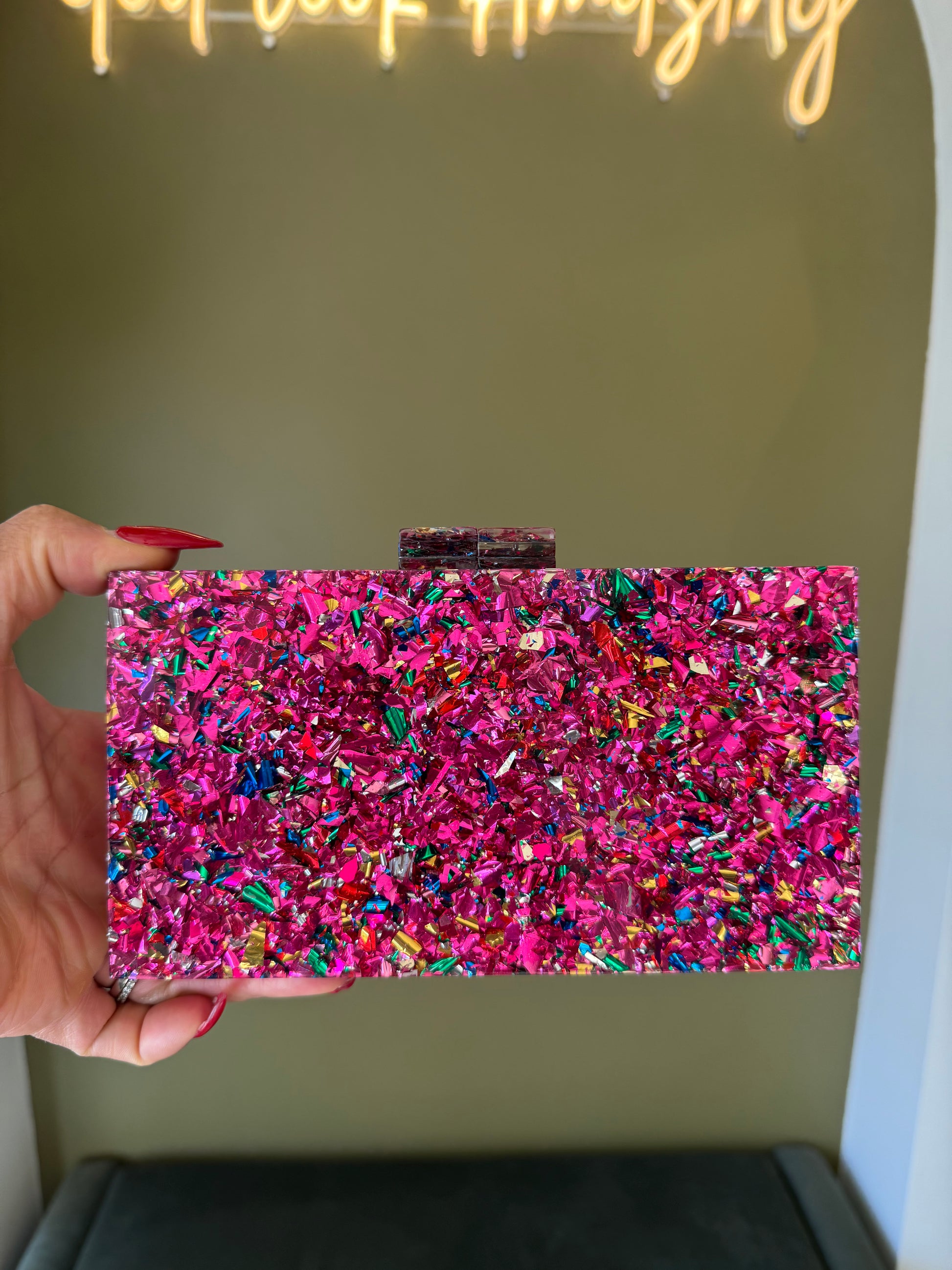 Rectangular pink acrylic clutch filled with vibrant multi-colored glitter confetti and a secure top clasp closure.