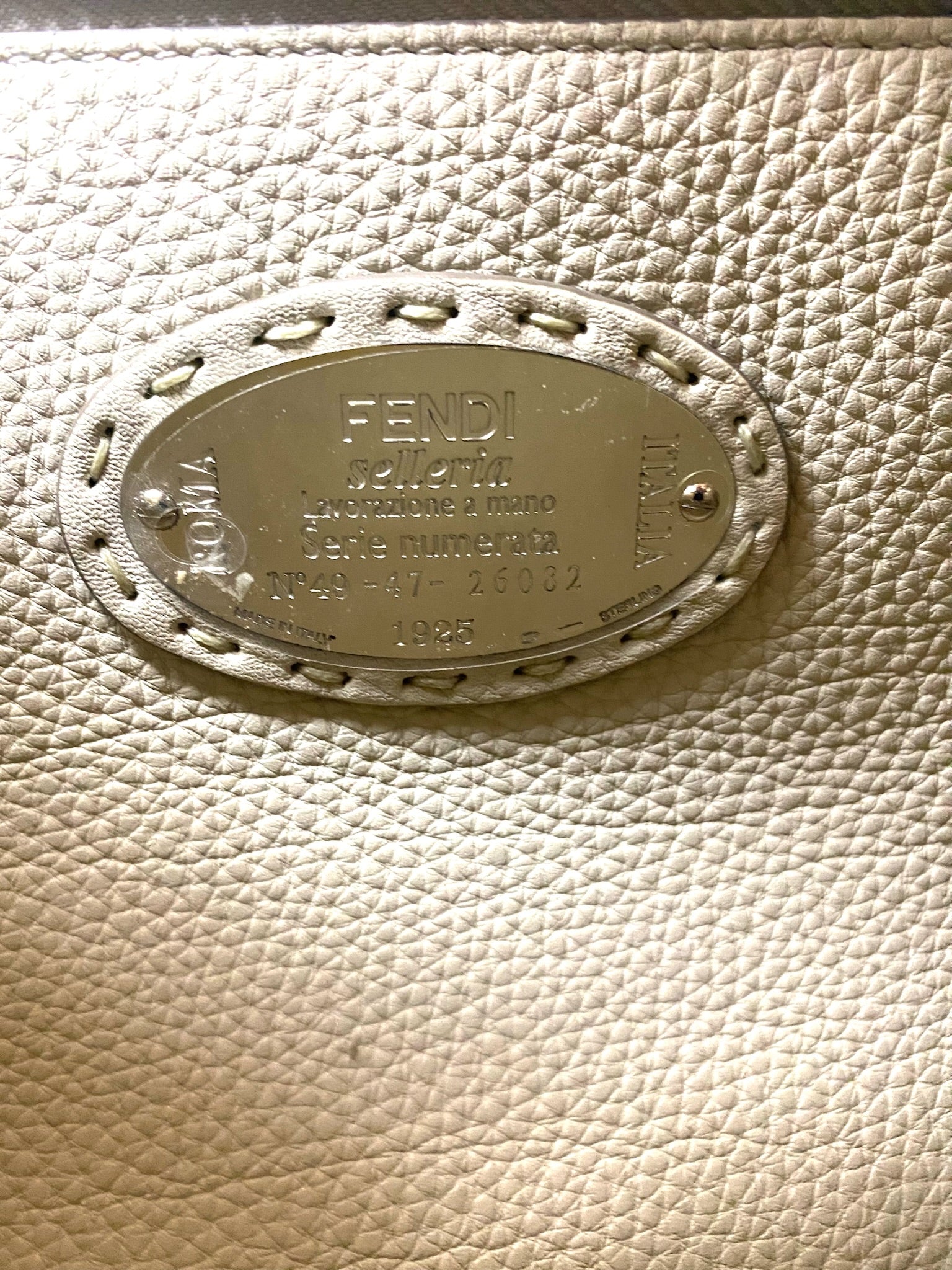 Close-up of Fendi Selleria leather with silver-tone brand plaque, serial number, and "ROMA ITALIA.