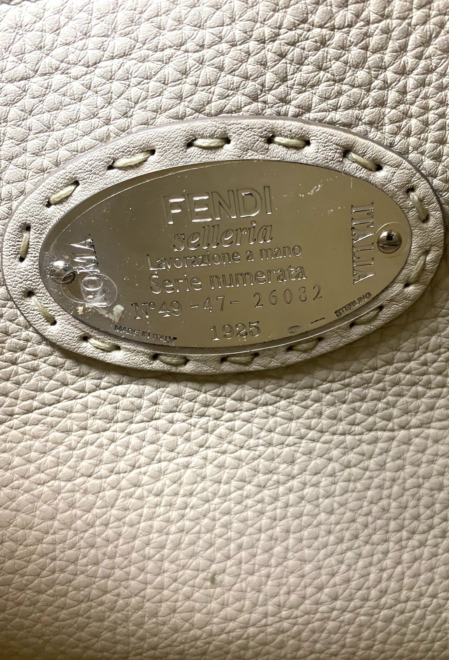 Close-up of Fendi Selleria leather bag's silver oval plaque with "FENDI selleria" engraving and serial number.