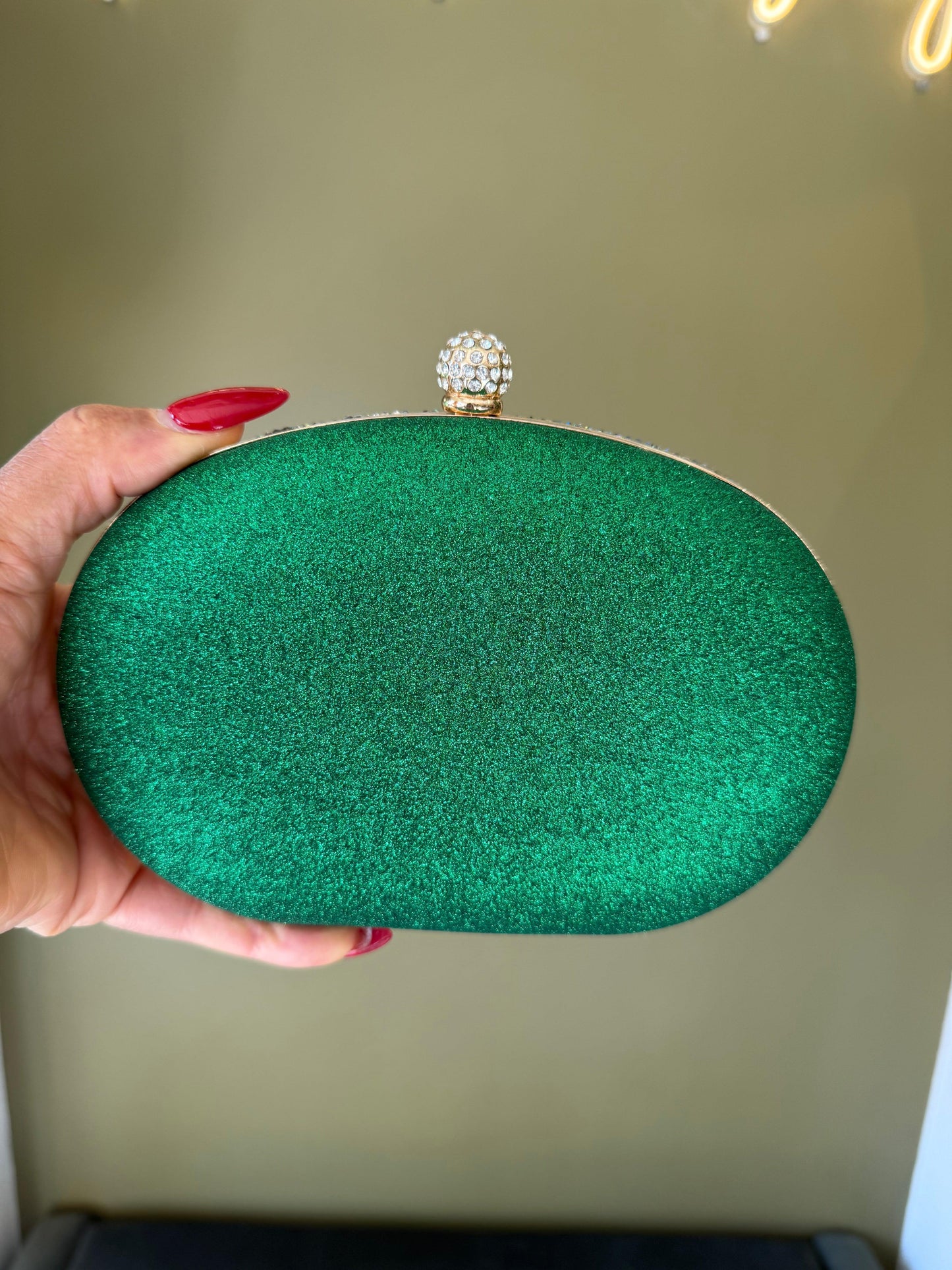 Emerald green glitter oval clutch with a gold frame and a sparkling rhinestone ball clasp held in a hand.