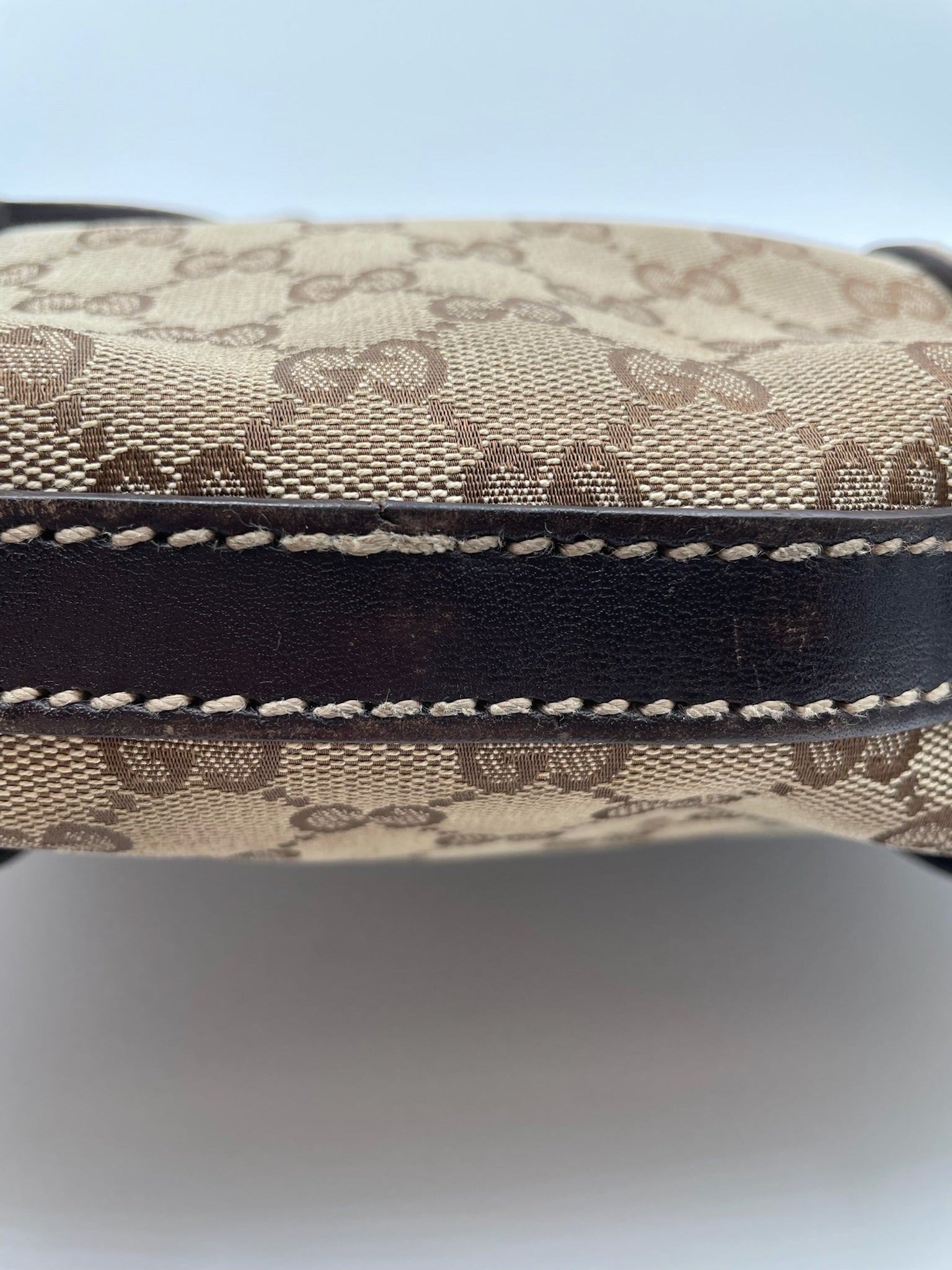 Close-up of beige and brown Gucci GG canvas hobo bag with dark brown leather trim and detailed white stitching.
