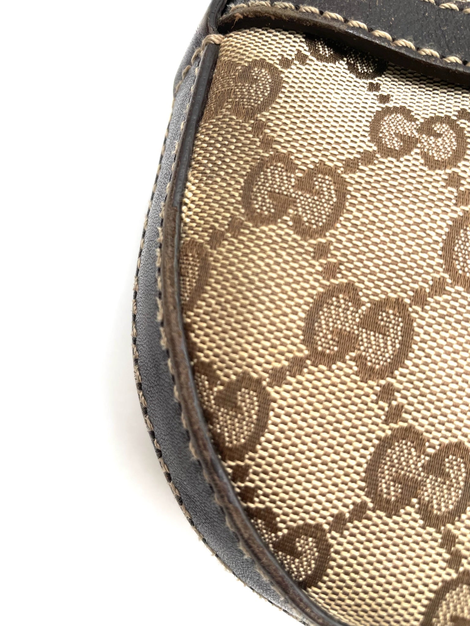 Close-up of beige and brown Gucci GG canvas hobo bag with dark brown leather trim and contrast stitching.