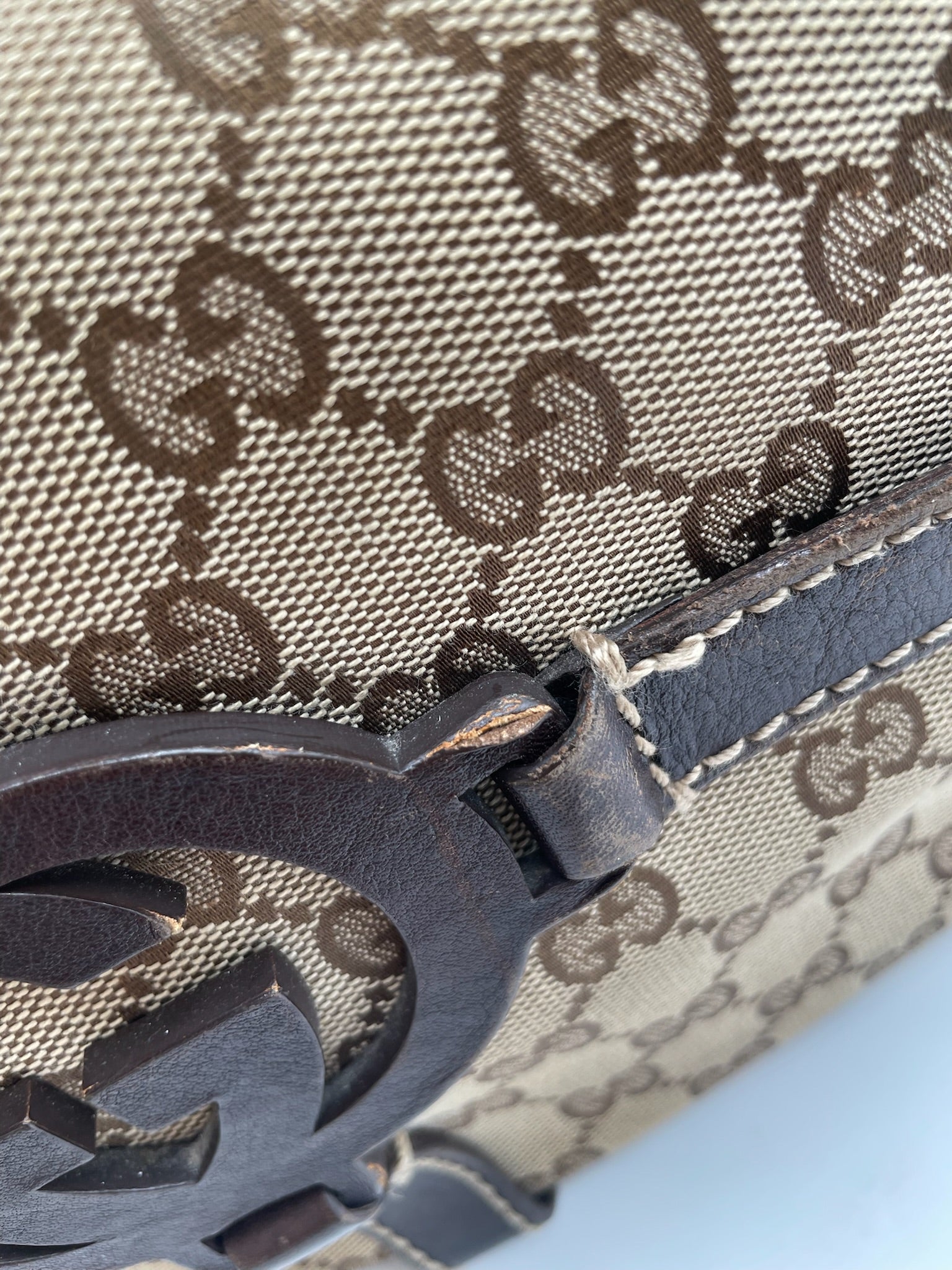 Close-up of beige and brown Gucci GG canvas hobo bag with dark brown leather trim and interlocking G logo detail.