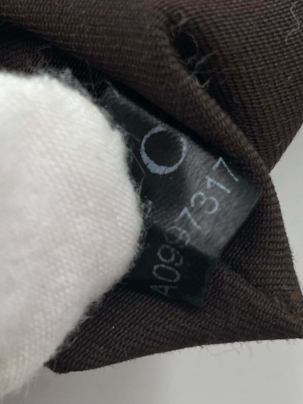 Gucci hobo bag interior black leather serial number tag with white text held by a gloved hand against brown fabric.