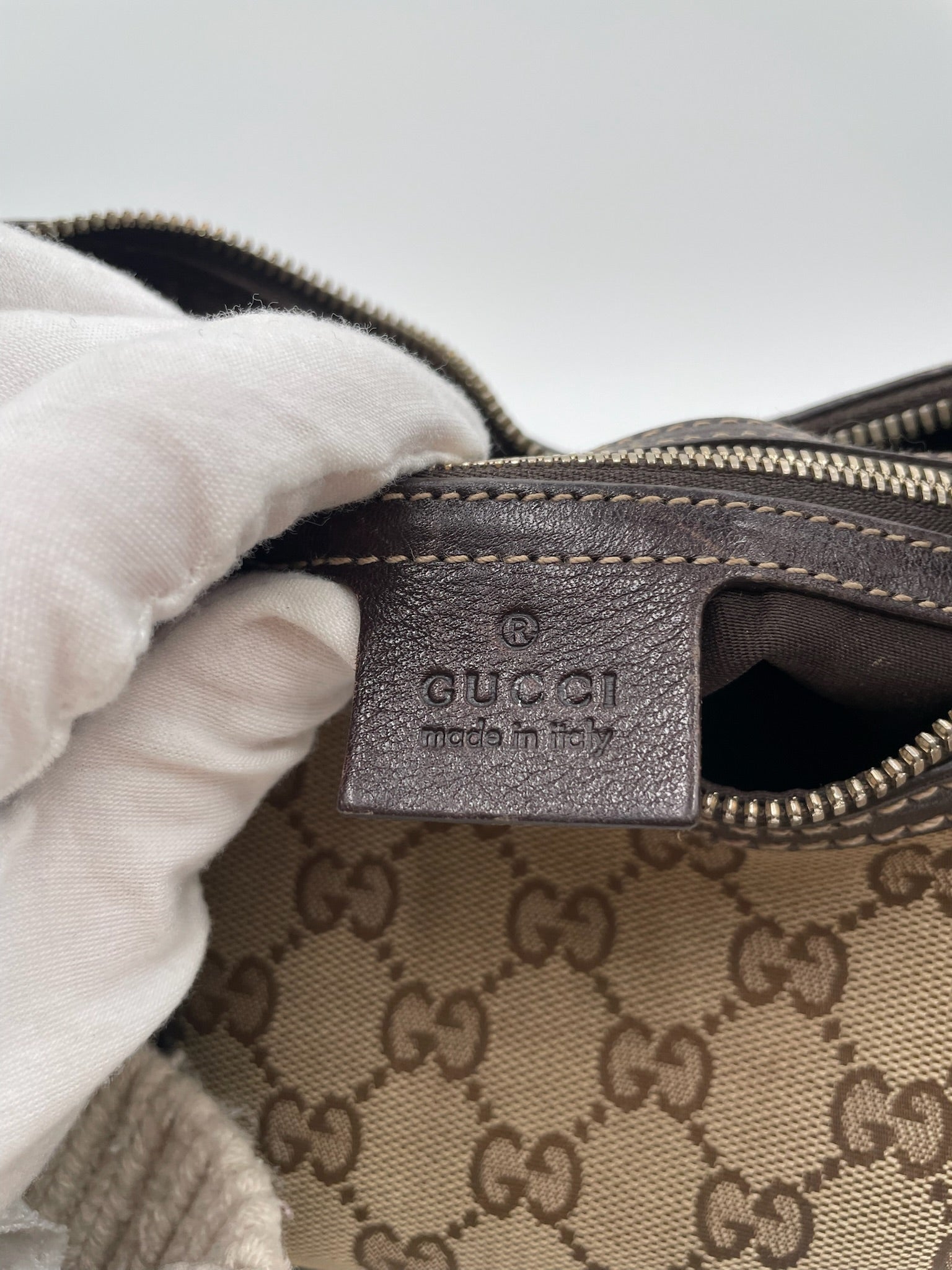 Close-up of a Gucci GG canvas hobo bag interior showing the embossed dark brown leather logo tag and zipper detail.