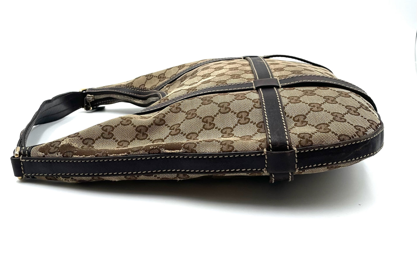 Gucci GG beige and brown canvas hobo bag with dark brown leather trim and top zip closure on a white background.
