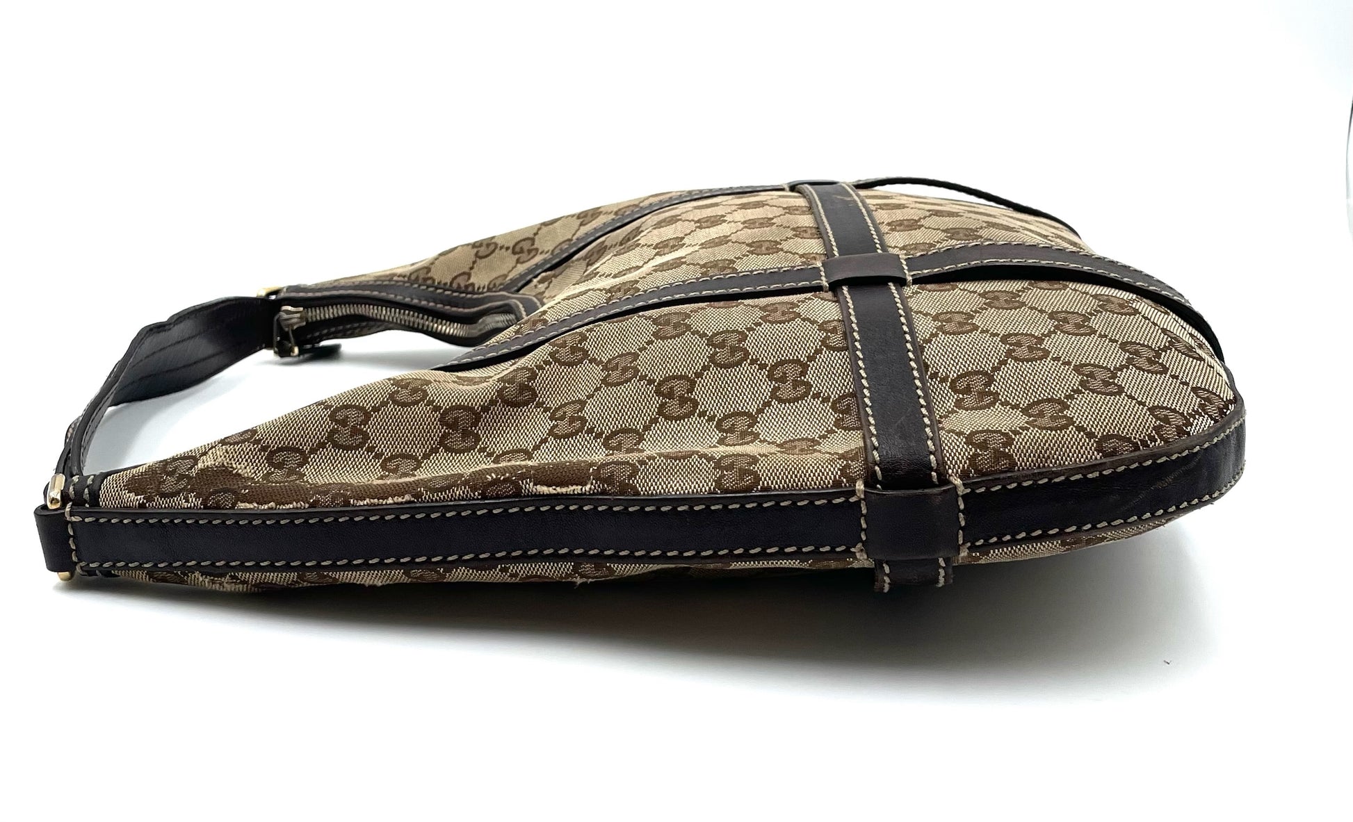 Gucci GG beige and brown canvas hobo bag with dark brown leather trim and top zip closure on a white background.