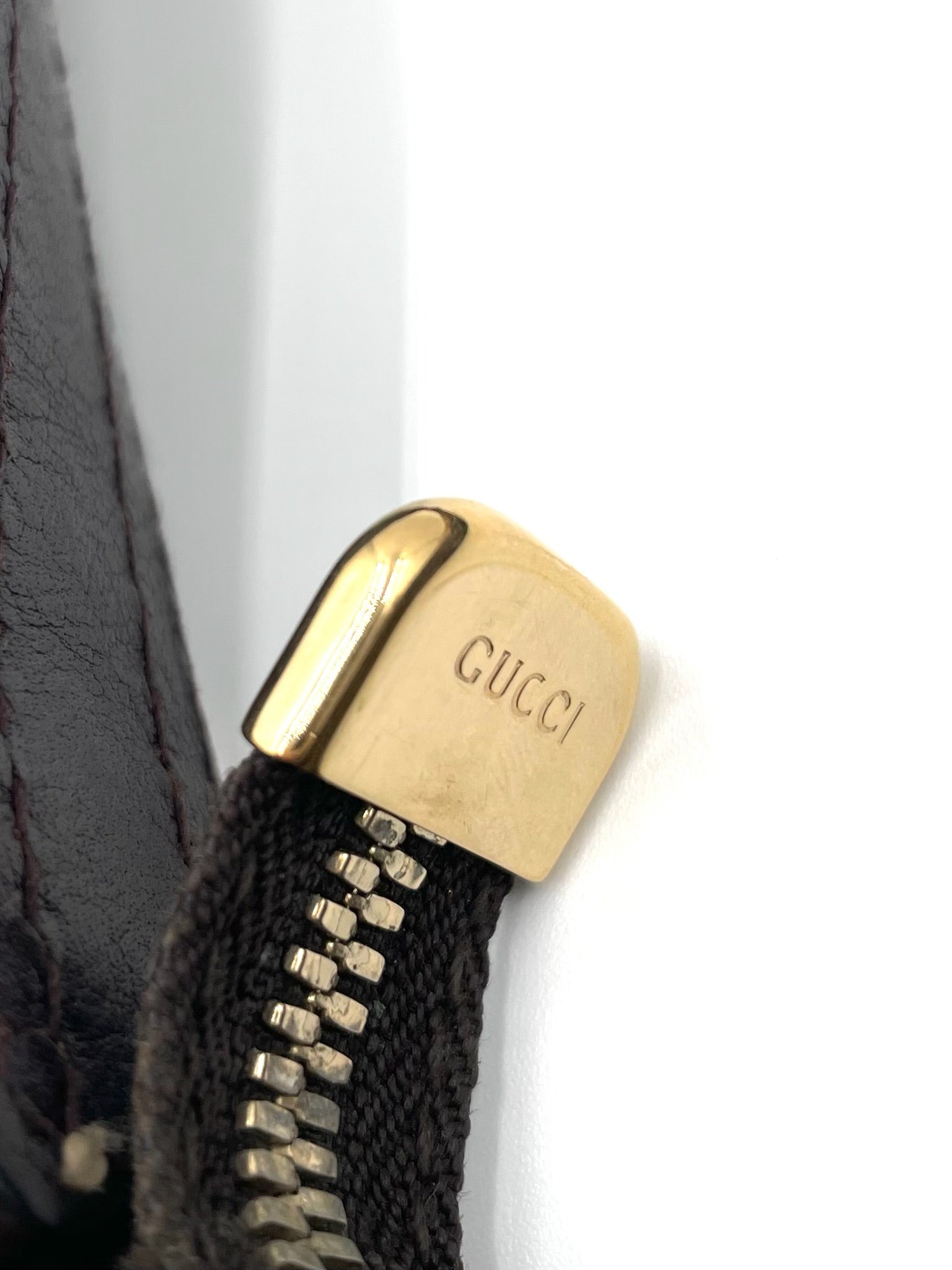 Gold-tone Gucci engraved zipper pull on a dark brown leather trimmed hobo bag.