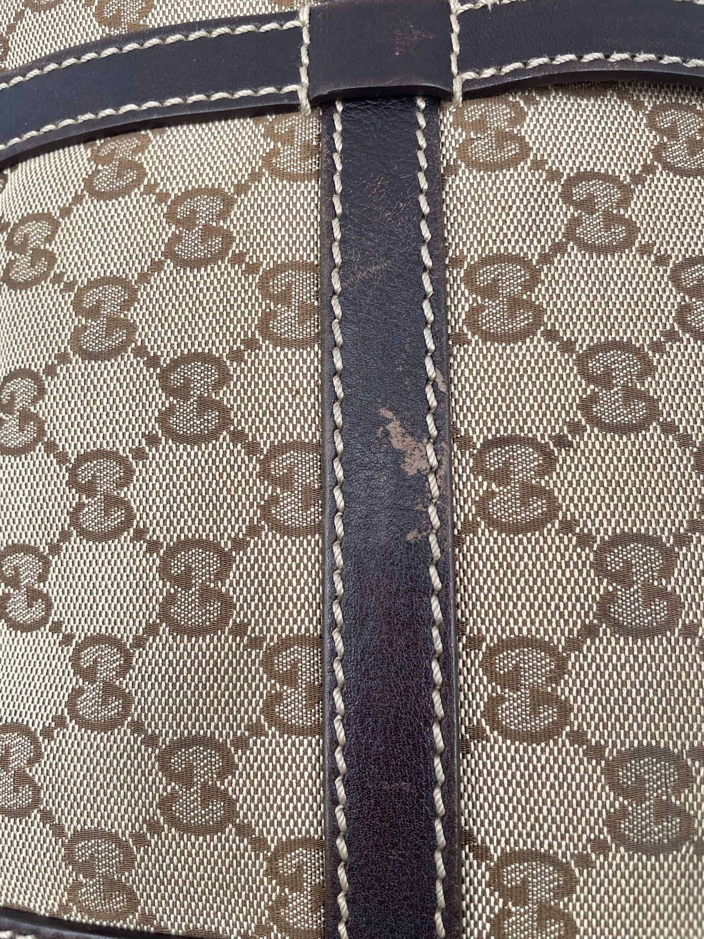 Close-up of beige and brown Gucci GG canvas hobo bag with dark brown leather trim and white contrast stitching.