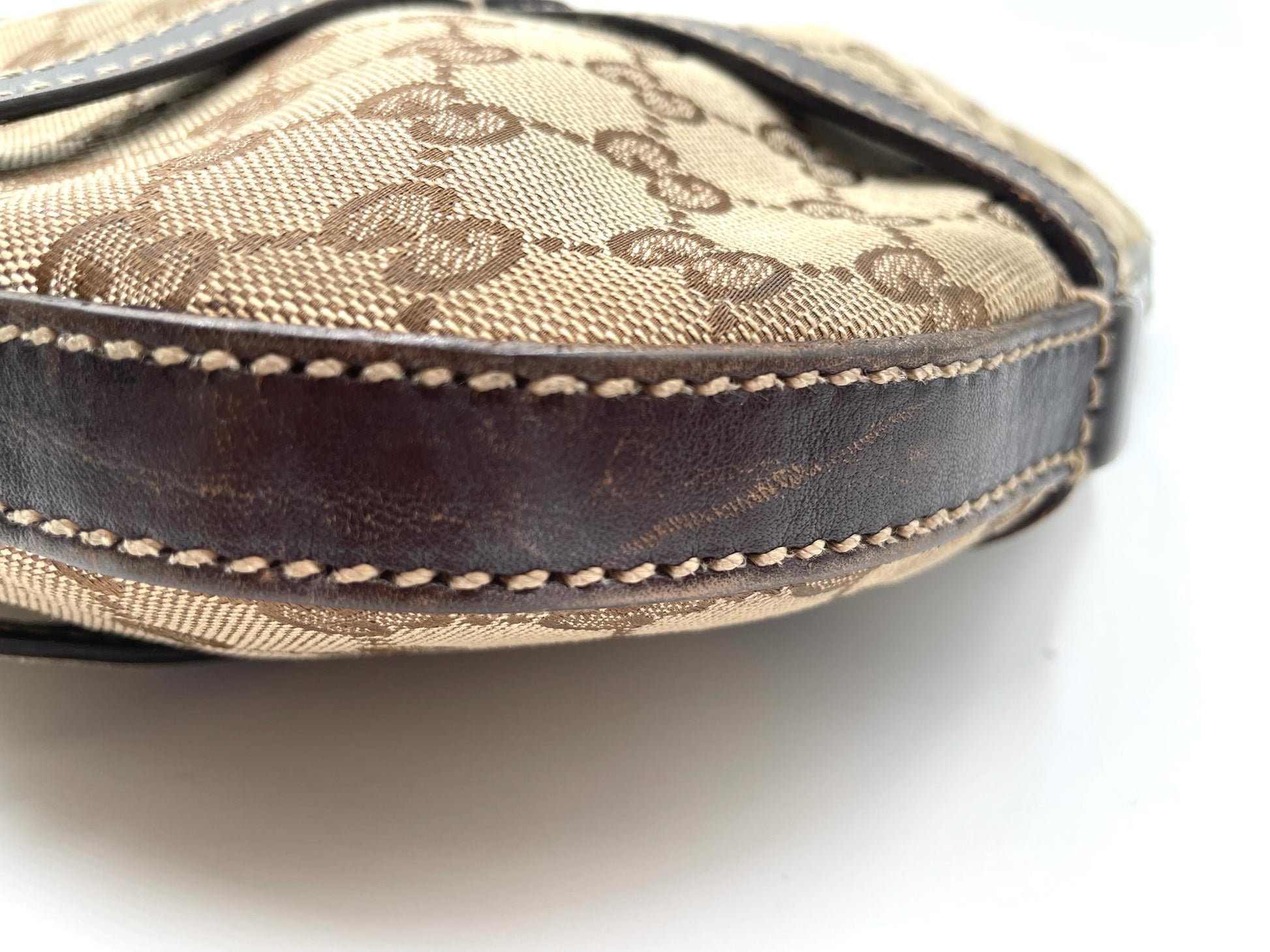 Close-up of beige Gucci GG canvas hobo bag with dark brown leather trim and detailed contrast stitching.