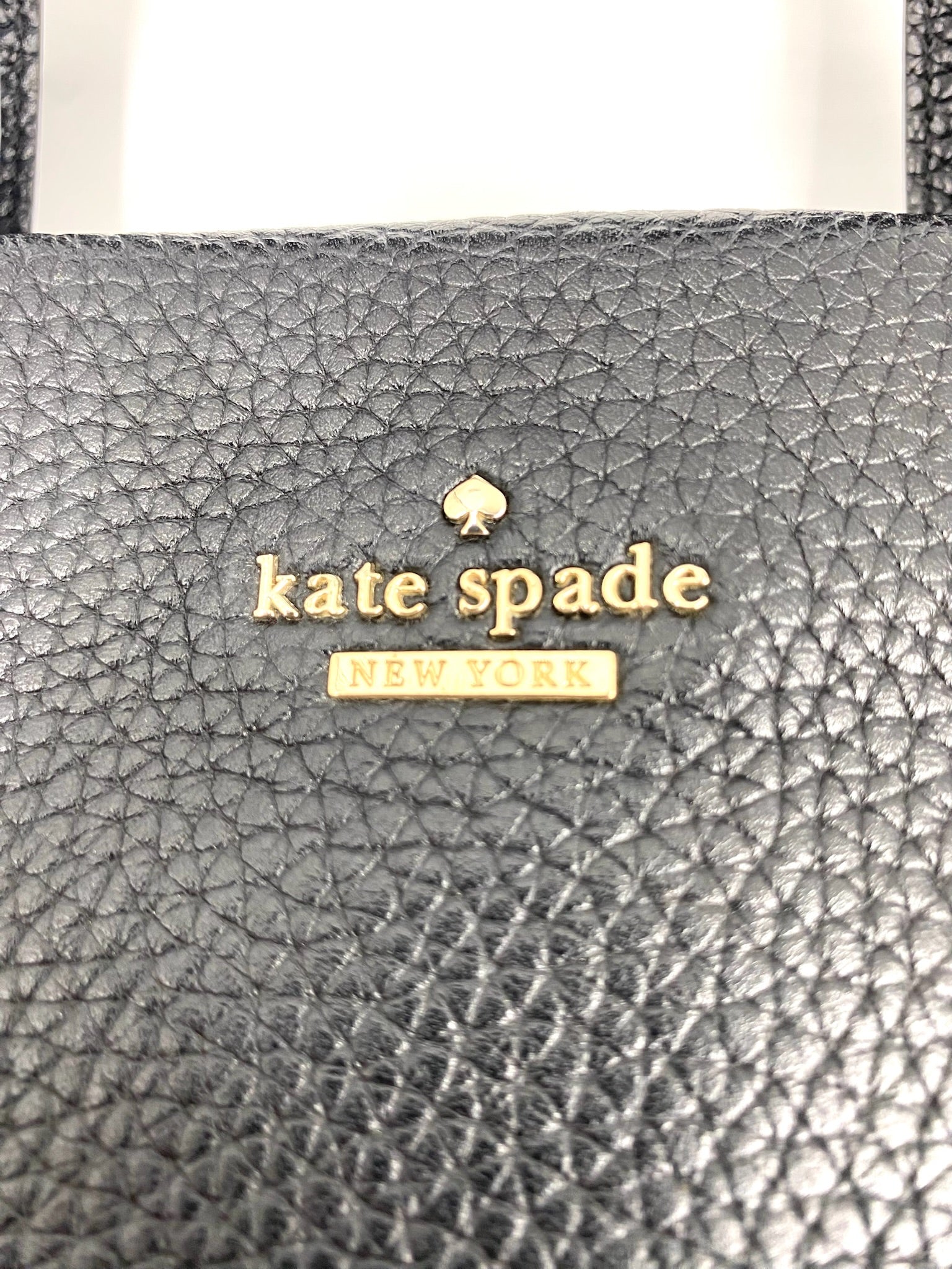 Close-up of a black pebbled leather Kate Spade New York tote bag with gold logo.