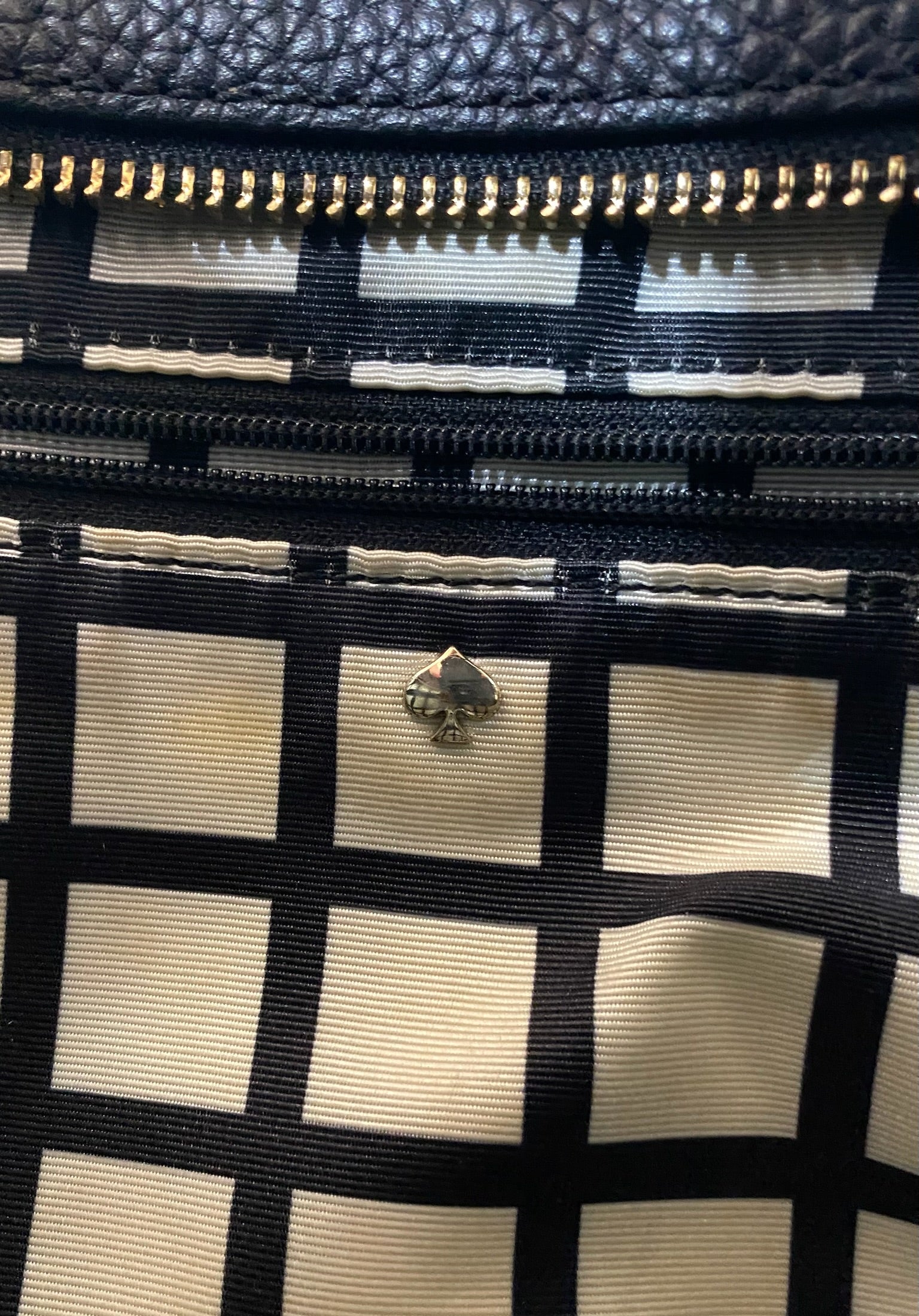 Close-up of Kate Spade black leather tote interior with signature spade logo and black and white grid lining.