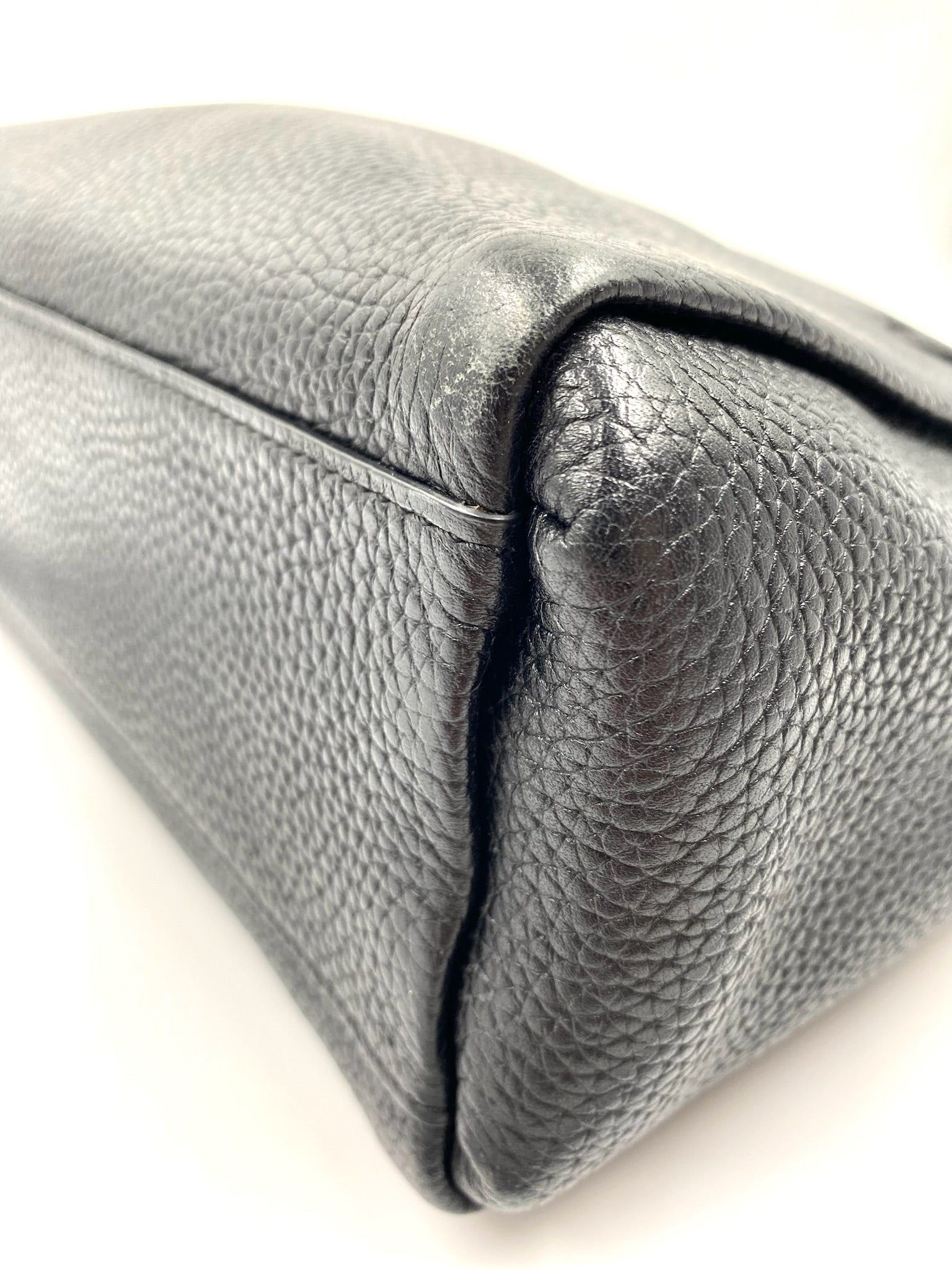 Close-up of a black pebbled leather Kate Spade tote bag, showing the textured material and corner stitching.