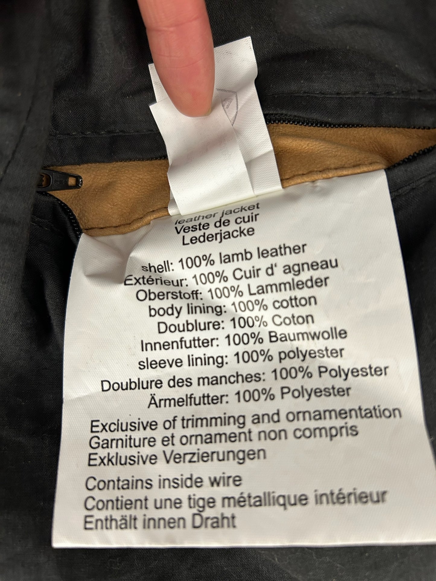 Close-up of a white clothing tag with black text detailing a brown lamb leather jacket's material composition.