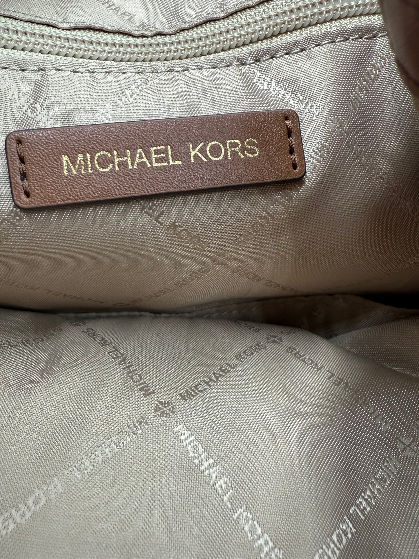 Close-up of the Michael Kors logo on a brown leather tag inside a beige monogrammed backpack.