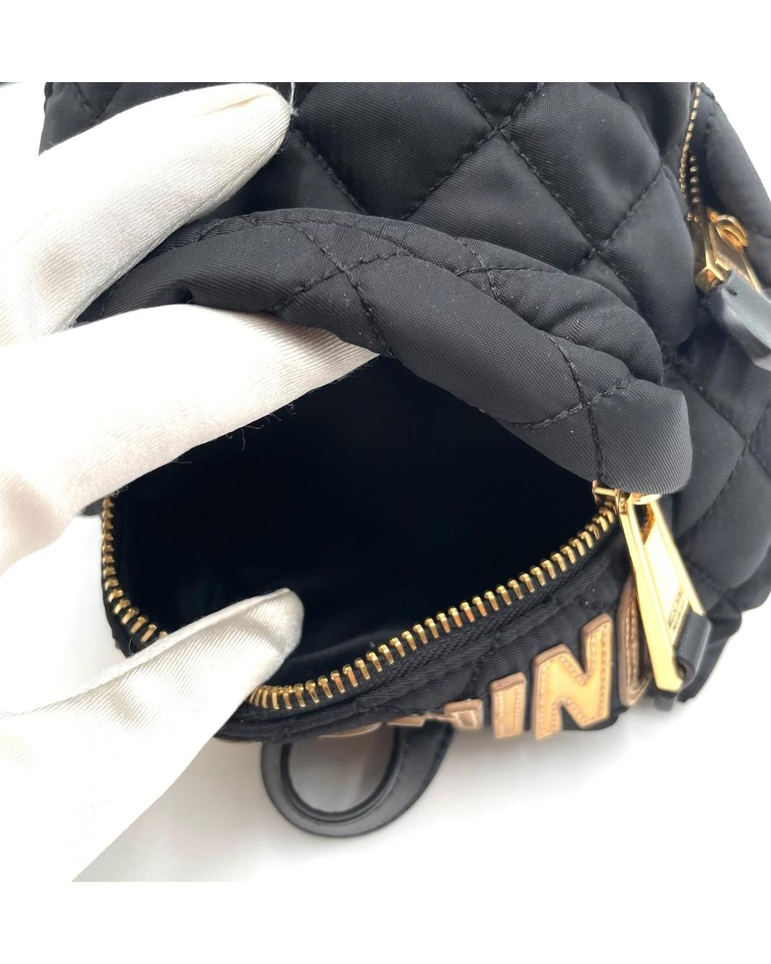 Black quilted nylon Moschino mini backpack with gold-tone zipper and logo detail, held by a gloved hand.