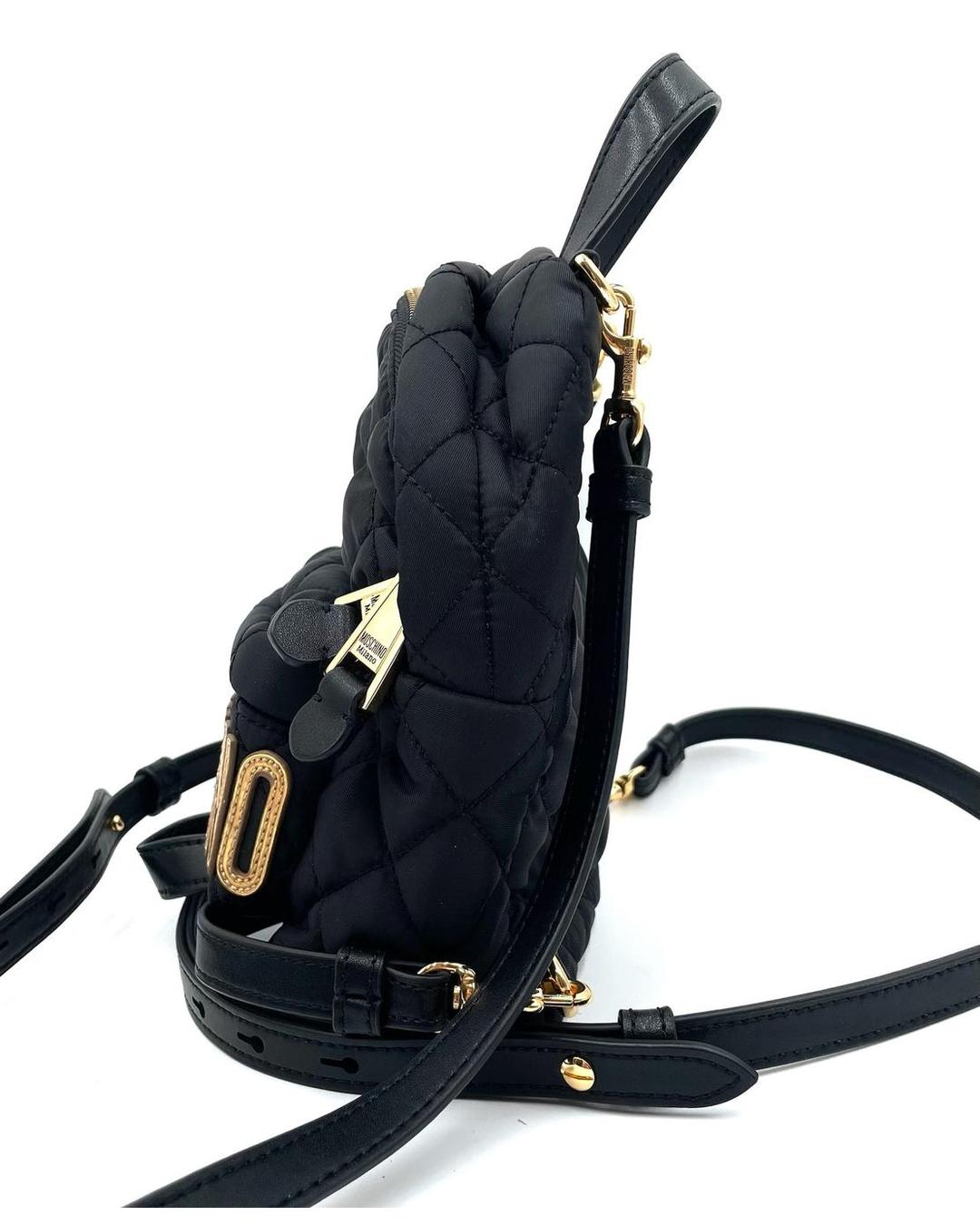 Side view of a black quilted nylon Moschino mini backpack with gold-tone logo hardware and detachable straps.