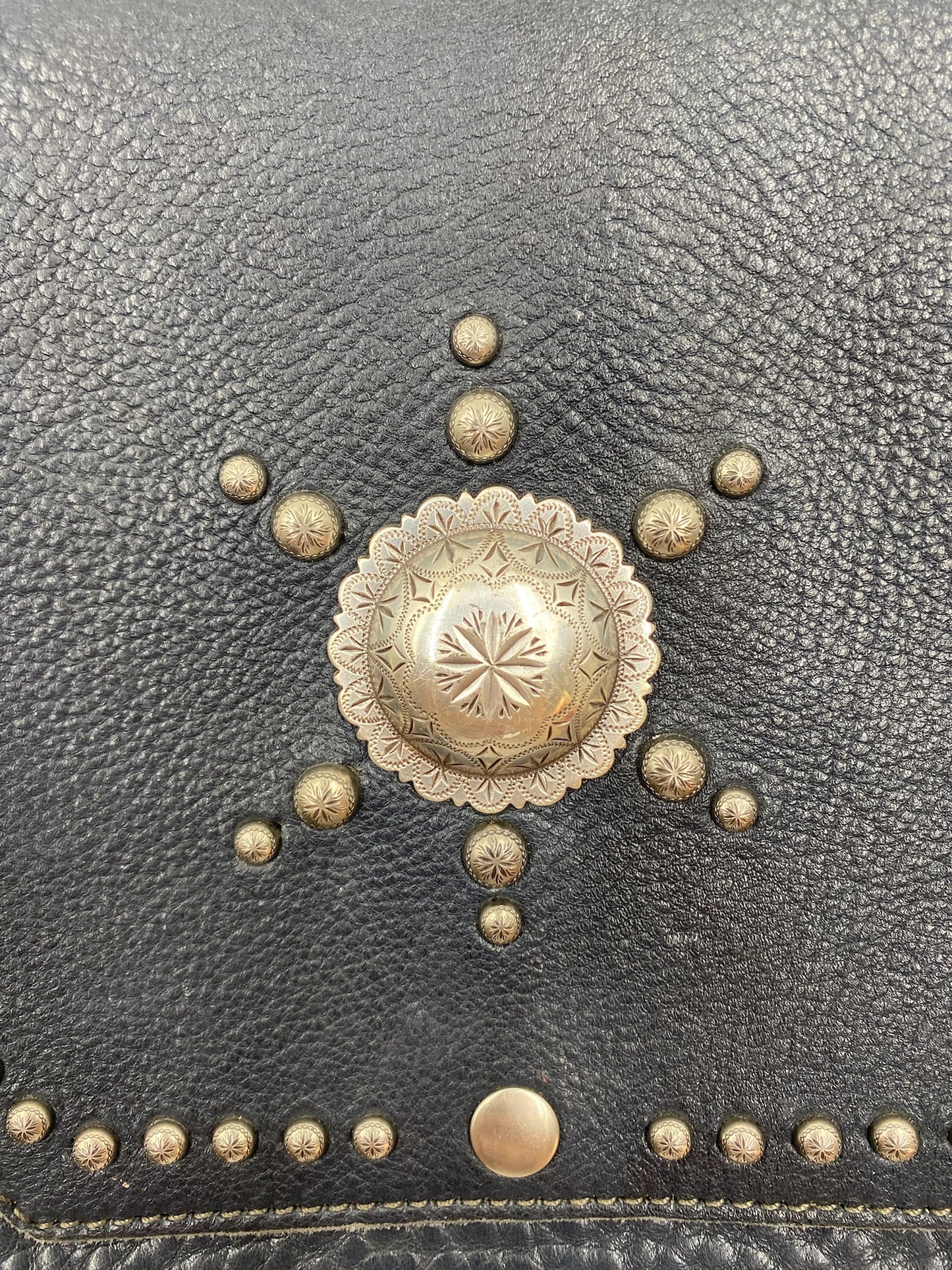 Close-up of a navy fringe leather crossbody bag with silver stud details and a large central concho.
