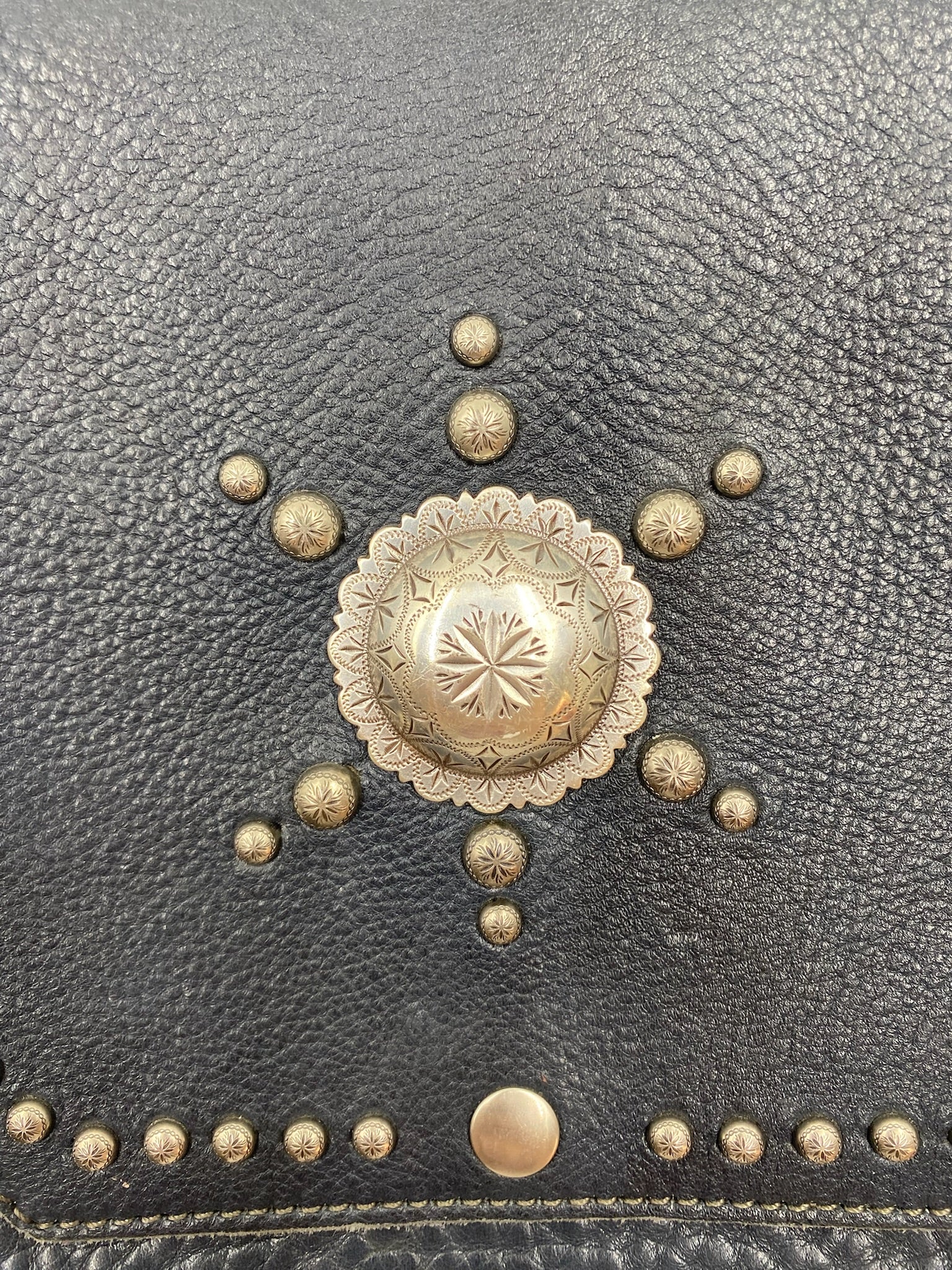 Close-up of a navy fringe leather crossbody bag with silver stud details and a large central concho.