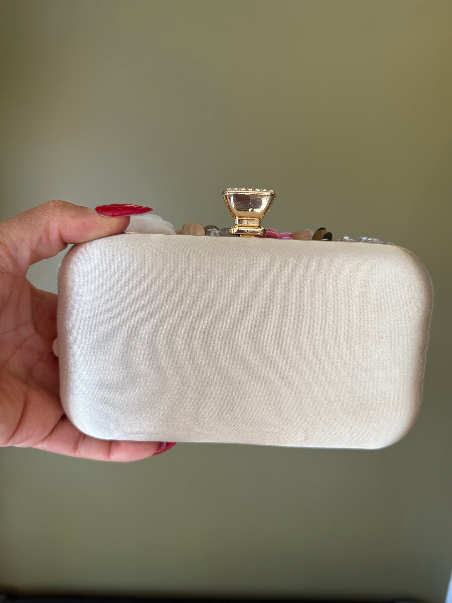 Satin pink clutch with a decorative rosette top, gold-tone crystal clasp, and a sleek rectangular hard-shell design.