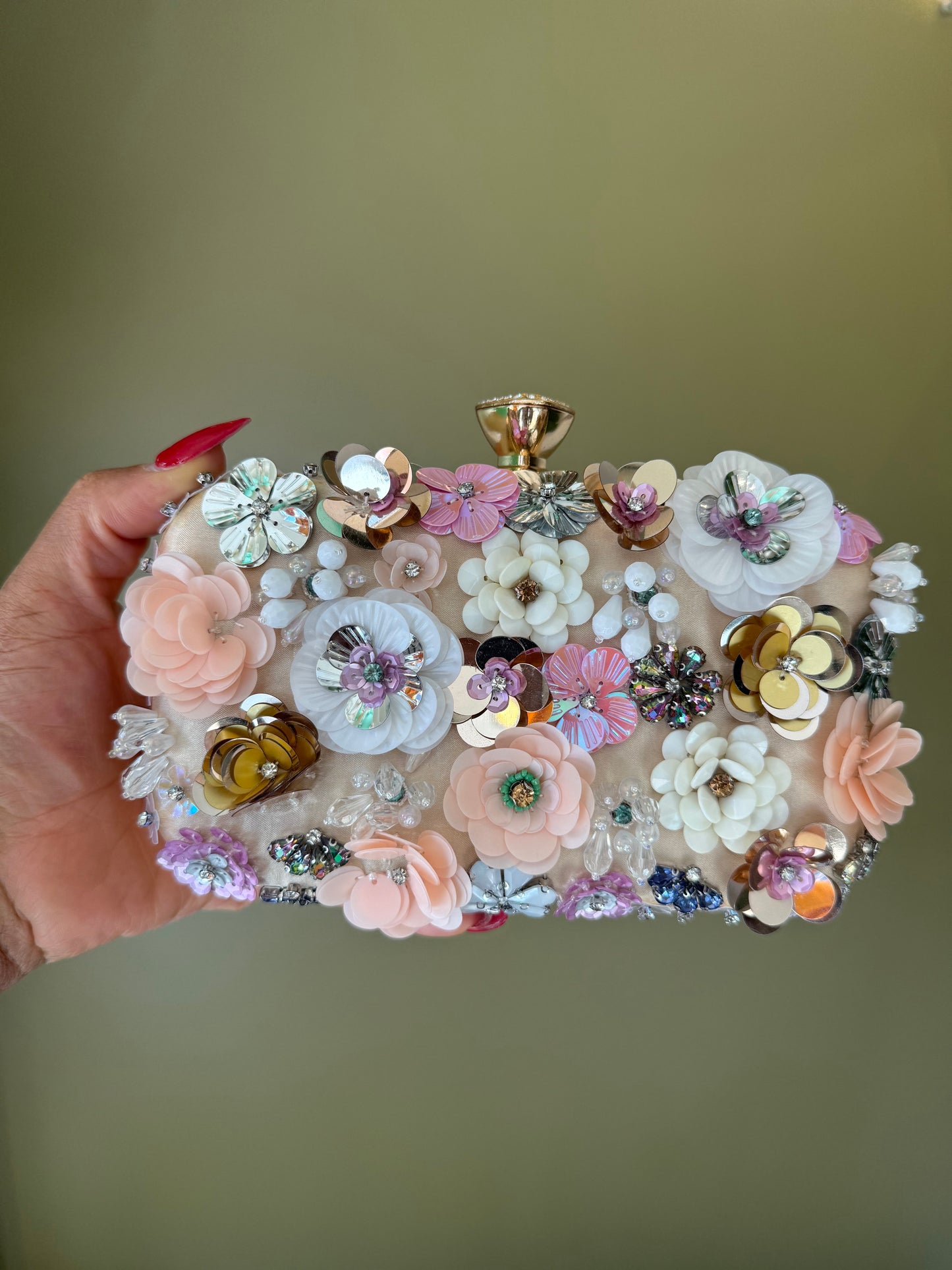 Pink satin clutch adorned with layered floral rosettes, iridescent sequins, and sparkling crystal accents with a gold clasp.