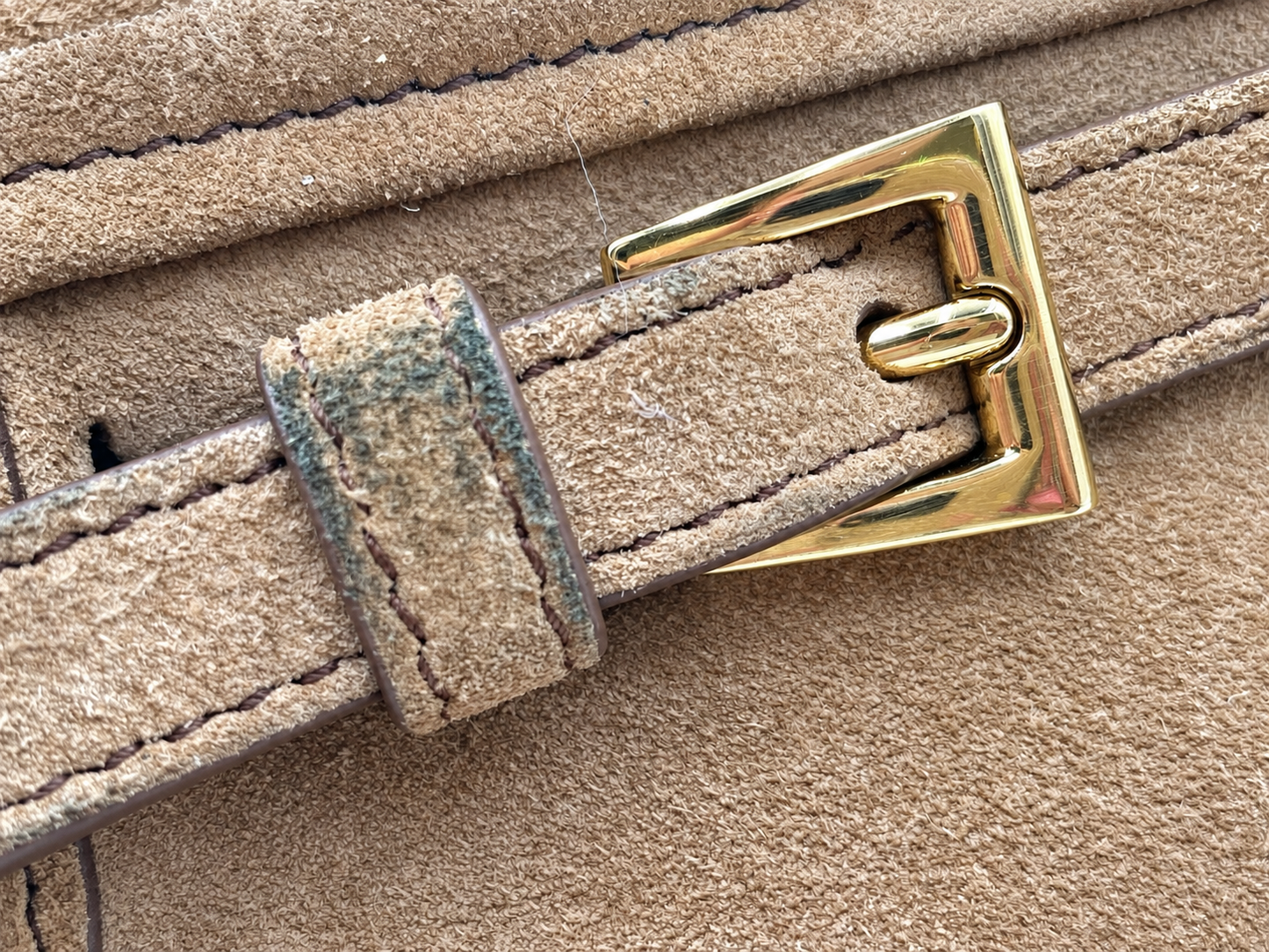 Close-up of a cinnamon brown suede Prada Bonnie bag strap featuring gold hardware and visible color transfer on the loop.
