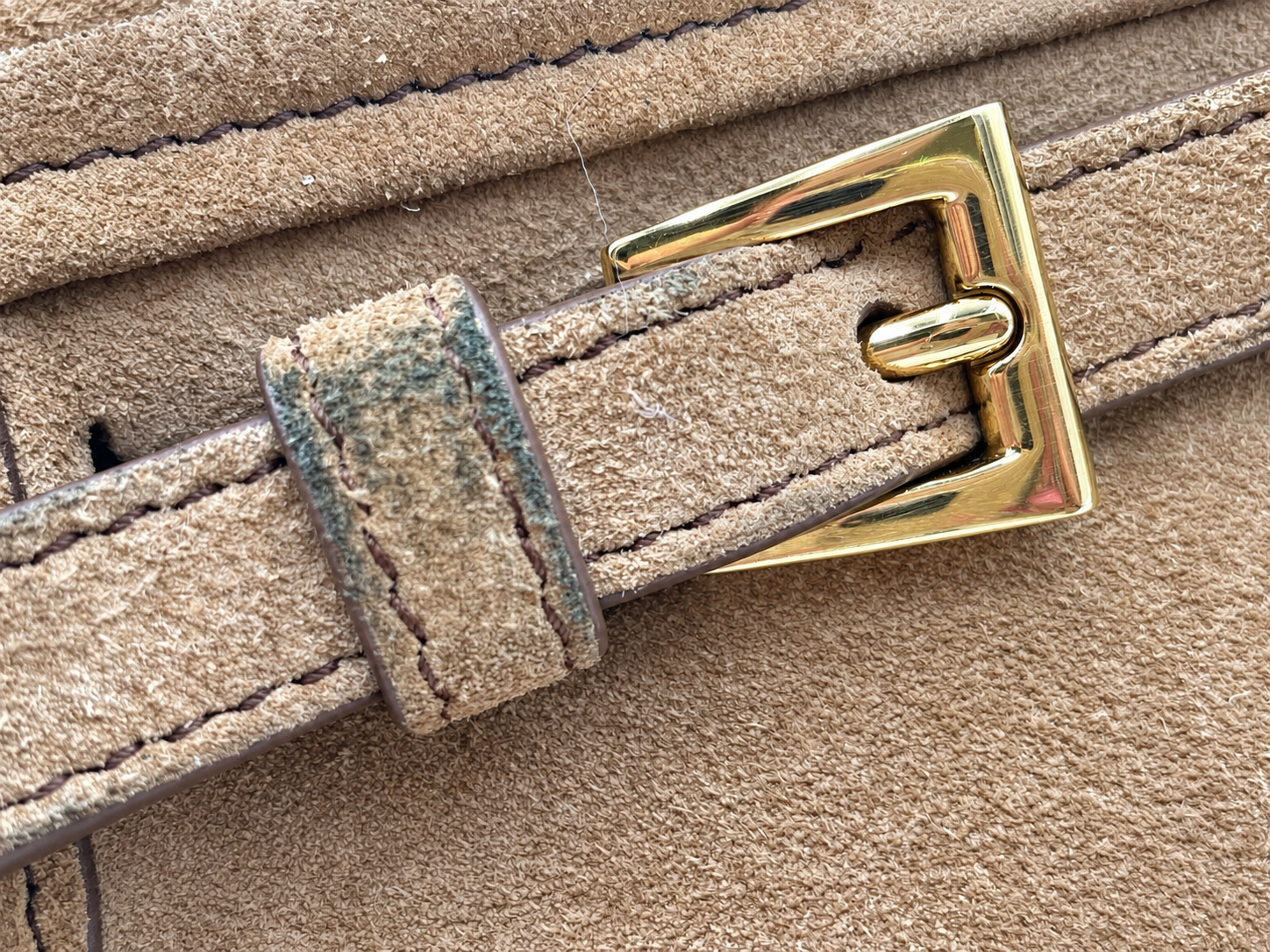 Close-up of a cinnamon brown suede Prada Bonnie bag strap featuring gold hardware and visible color transfer on the loop.